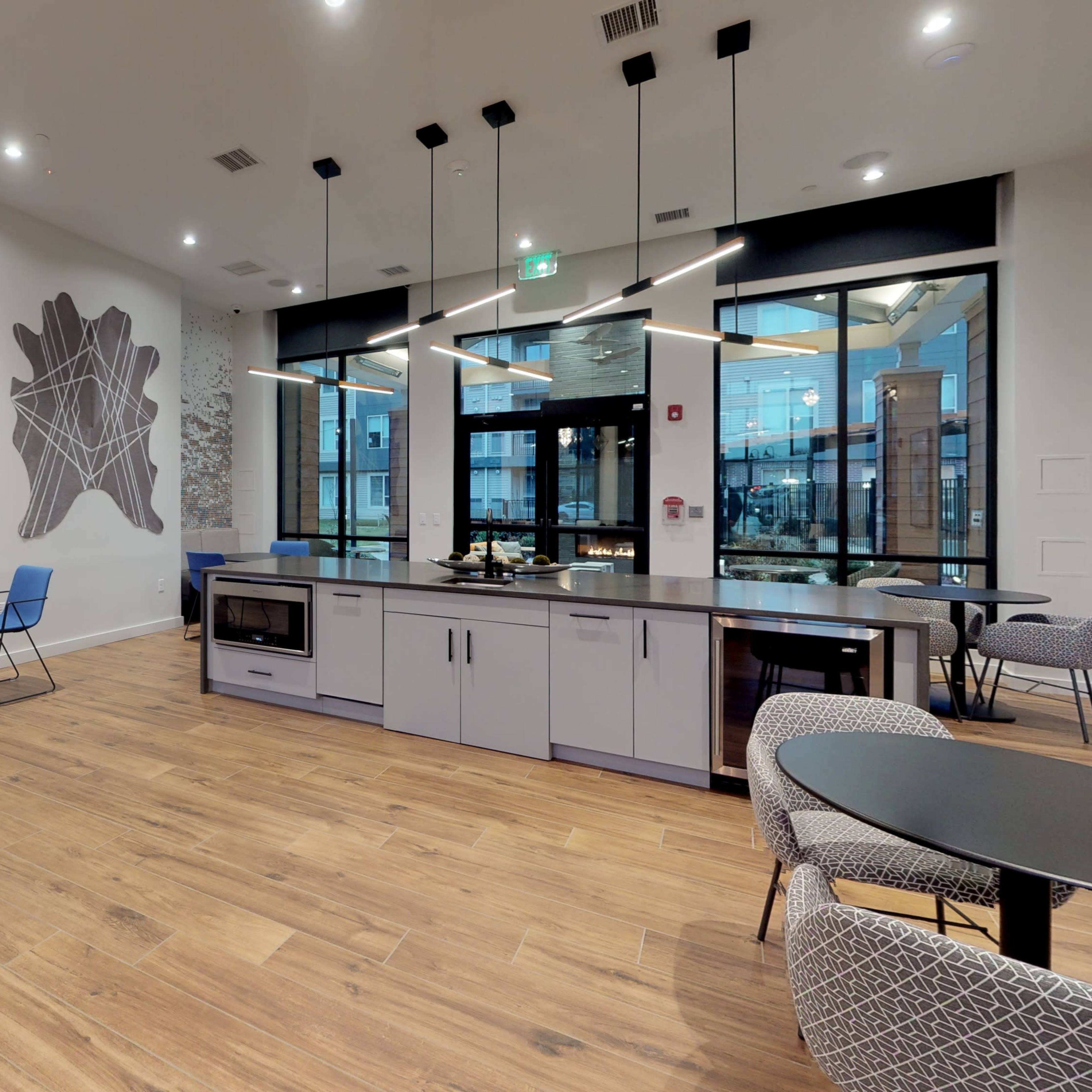 A modern communal space with kitchen amenities, seating areas, and large windows.