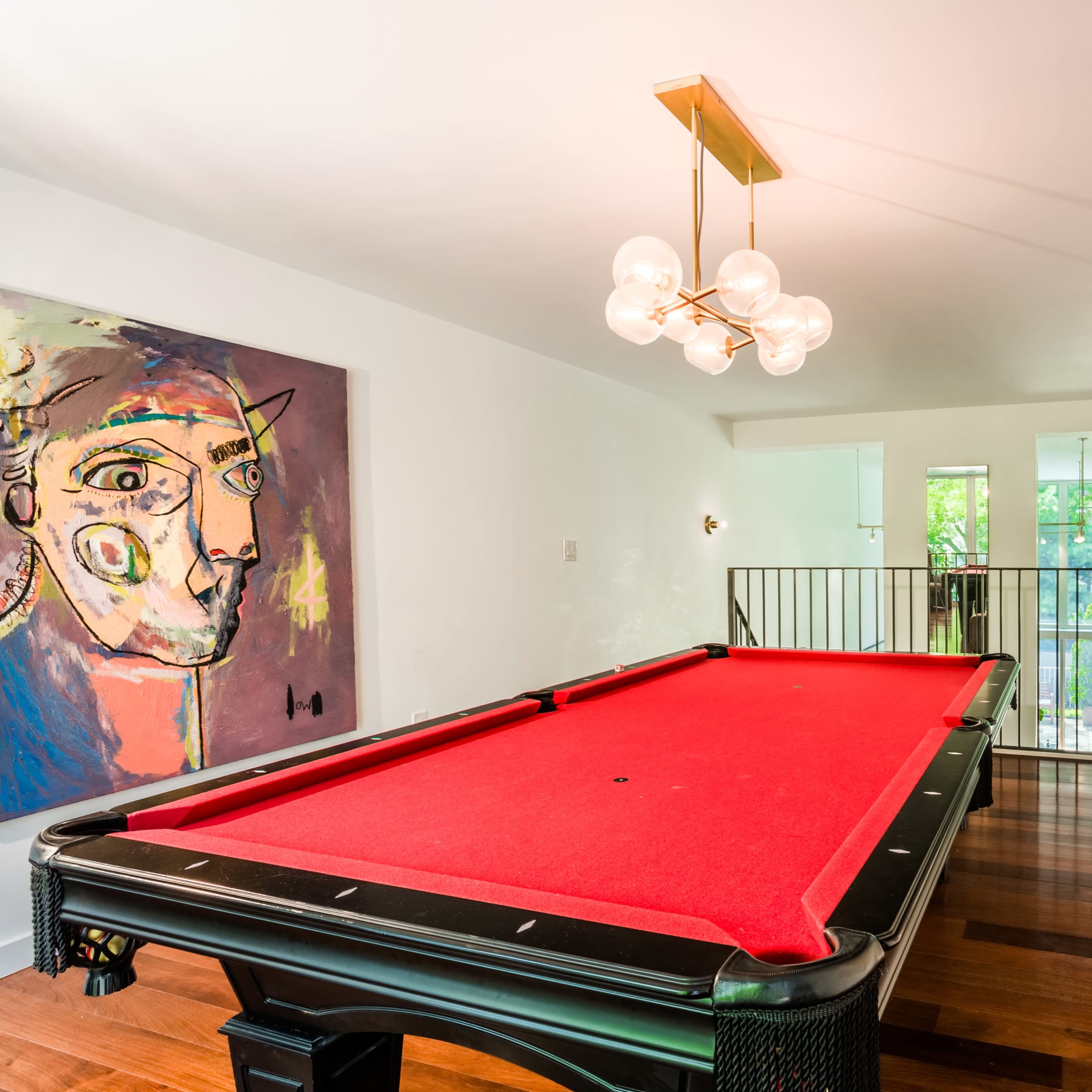 A brightly lit game room features a red pool table, modern lighting, and a large artwork on the wall.