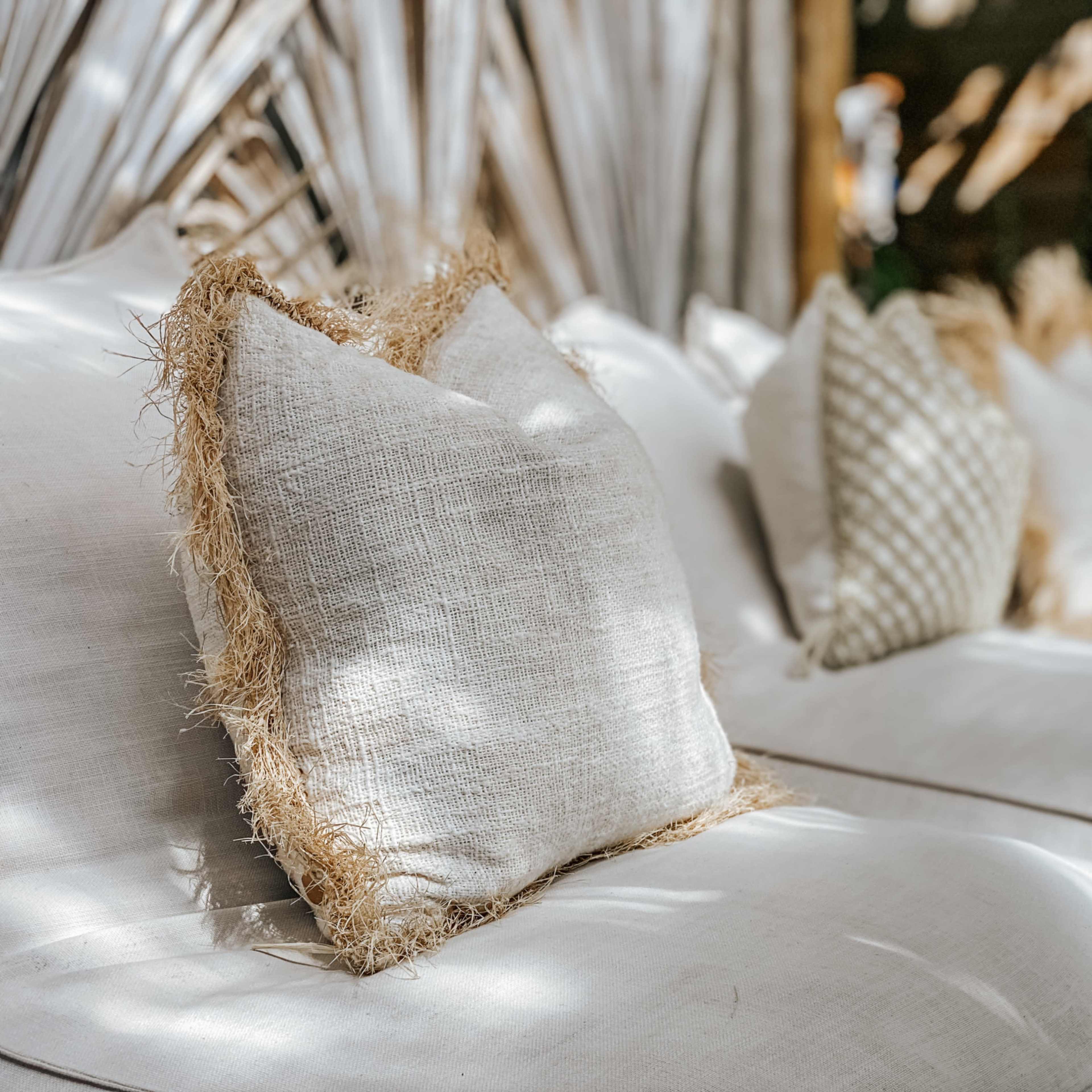 A beige couch with textured cushions is placed in a sunlit area surrounded by plants.
