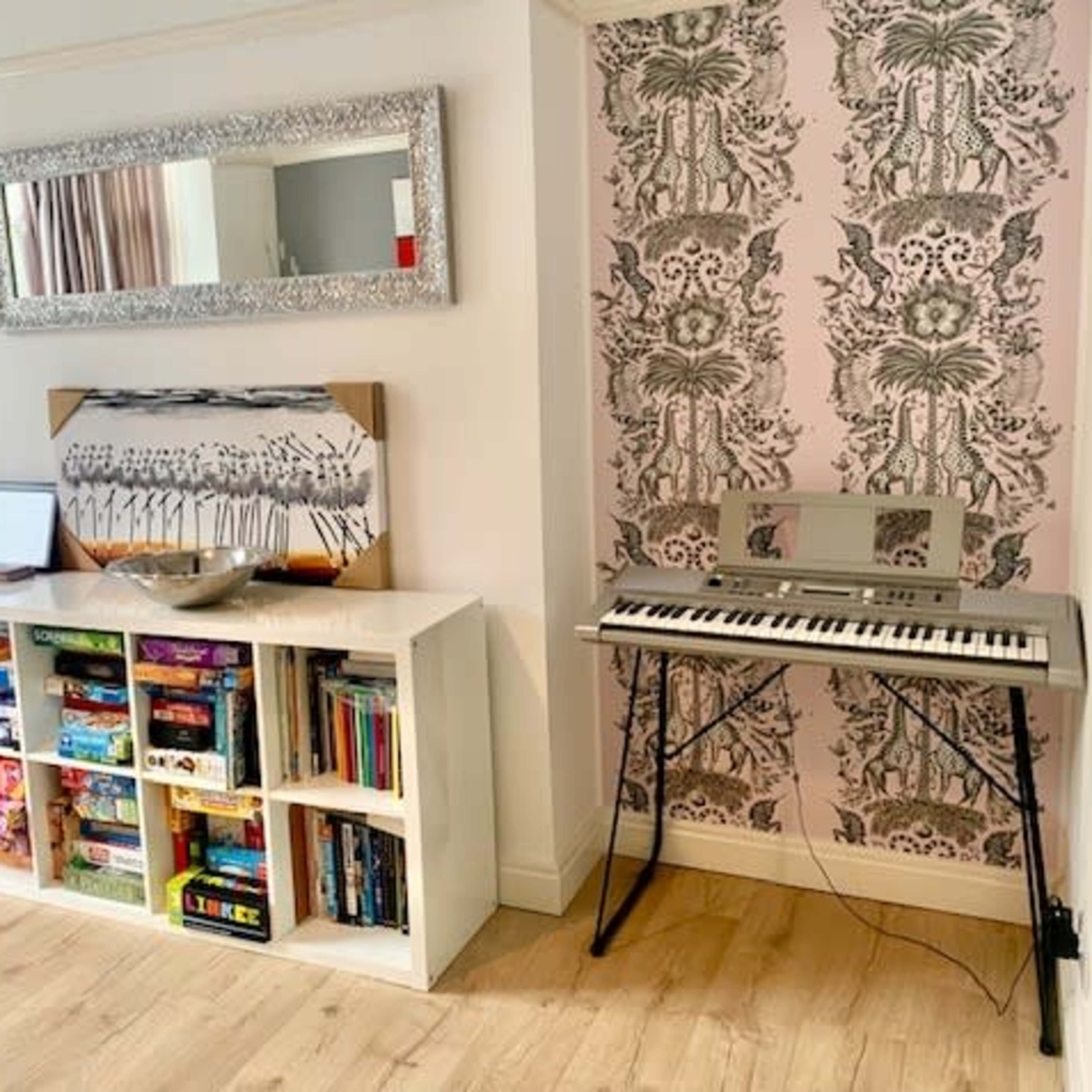 The room features a television on one side, a white shelving unit filled with books and games, and a keyboard on a stand against a patterned wall.