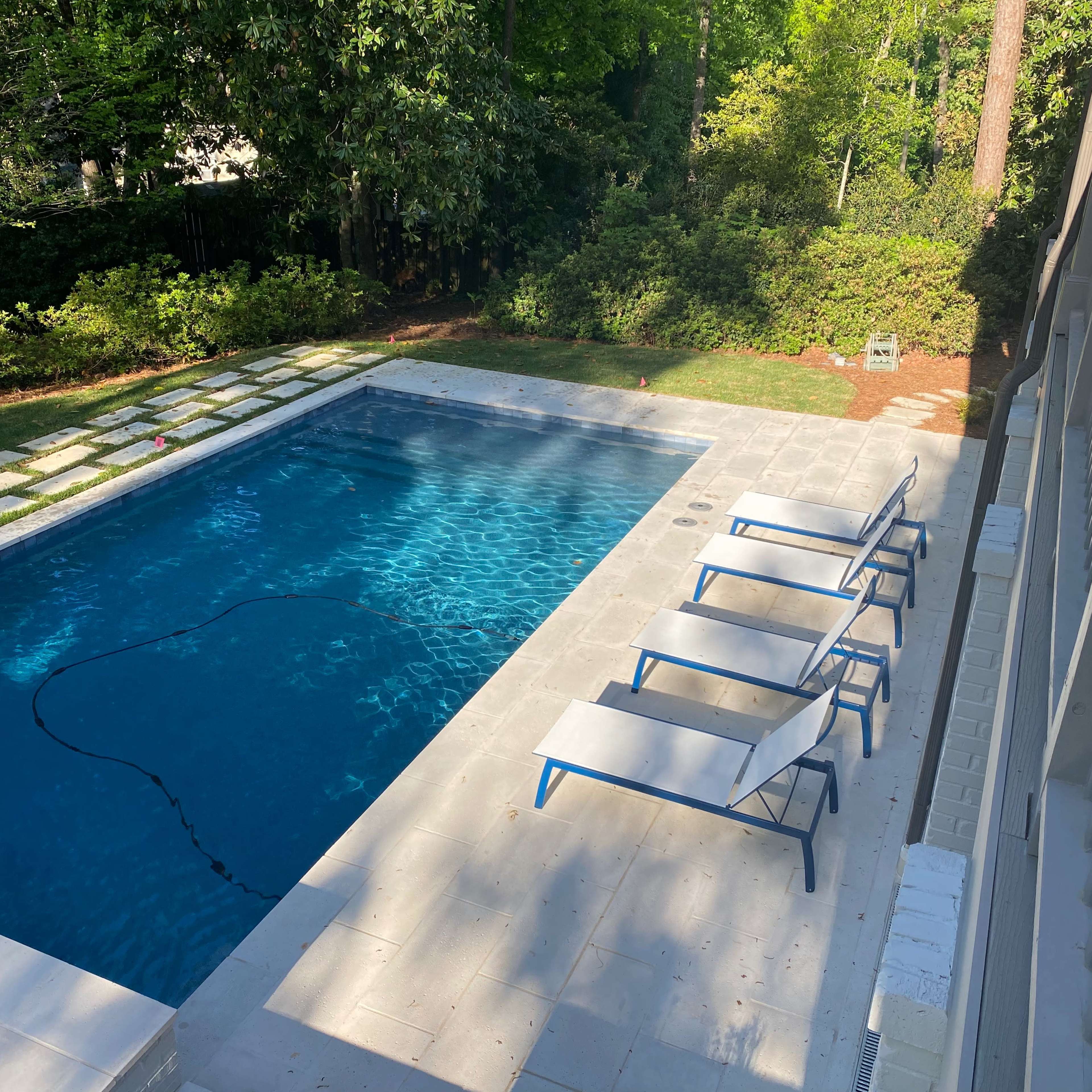 A backyard swimming pool surrounded by a stone patio and several lounge chairs.