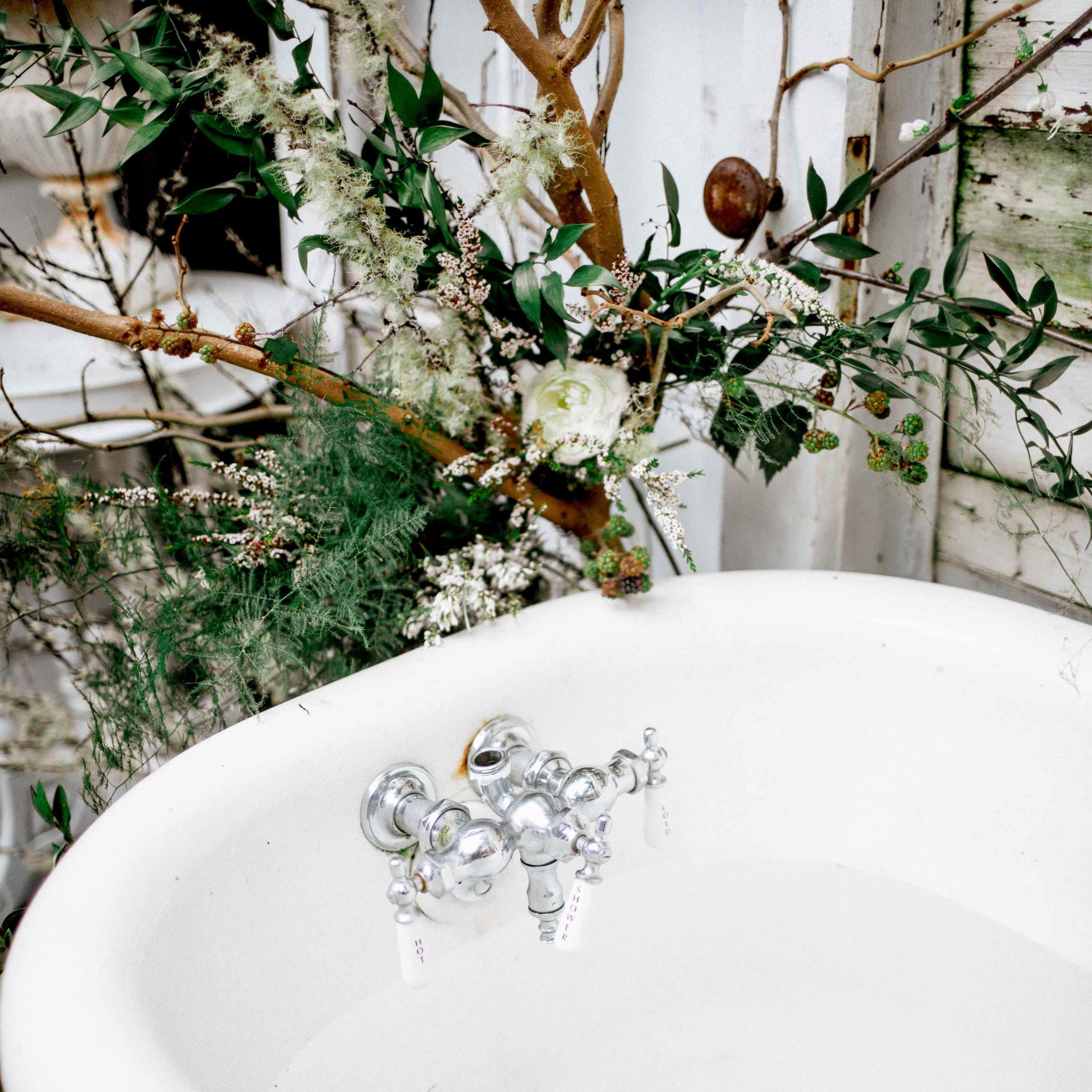 A vintage bathtub is positioned under a decorated arrangement of branches and flowers.