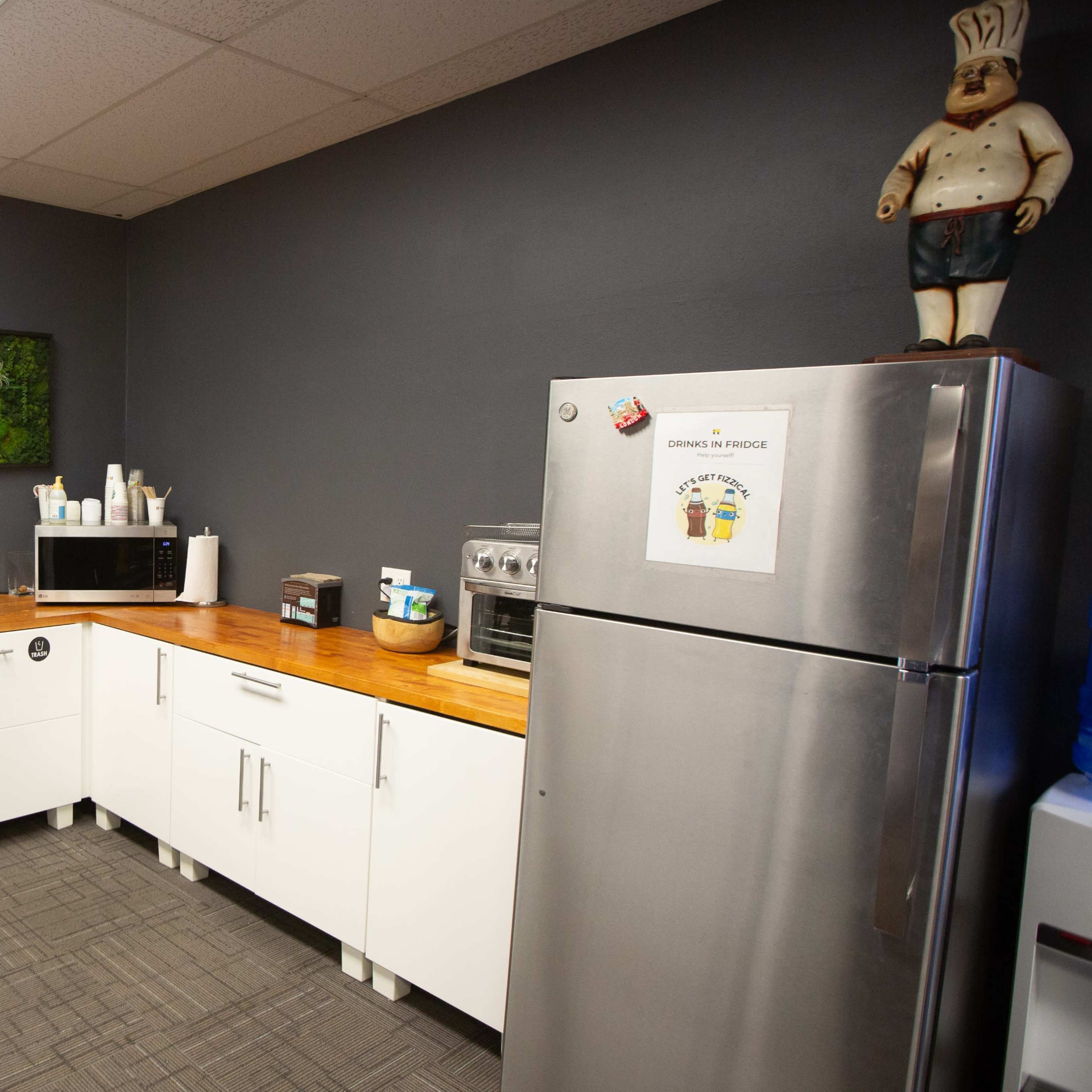 A kitchen area with a wooden countertop, a stainless steel refrigerator, and various appliances against a gray wall.