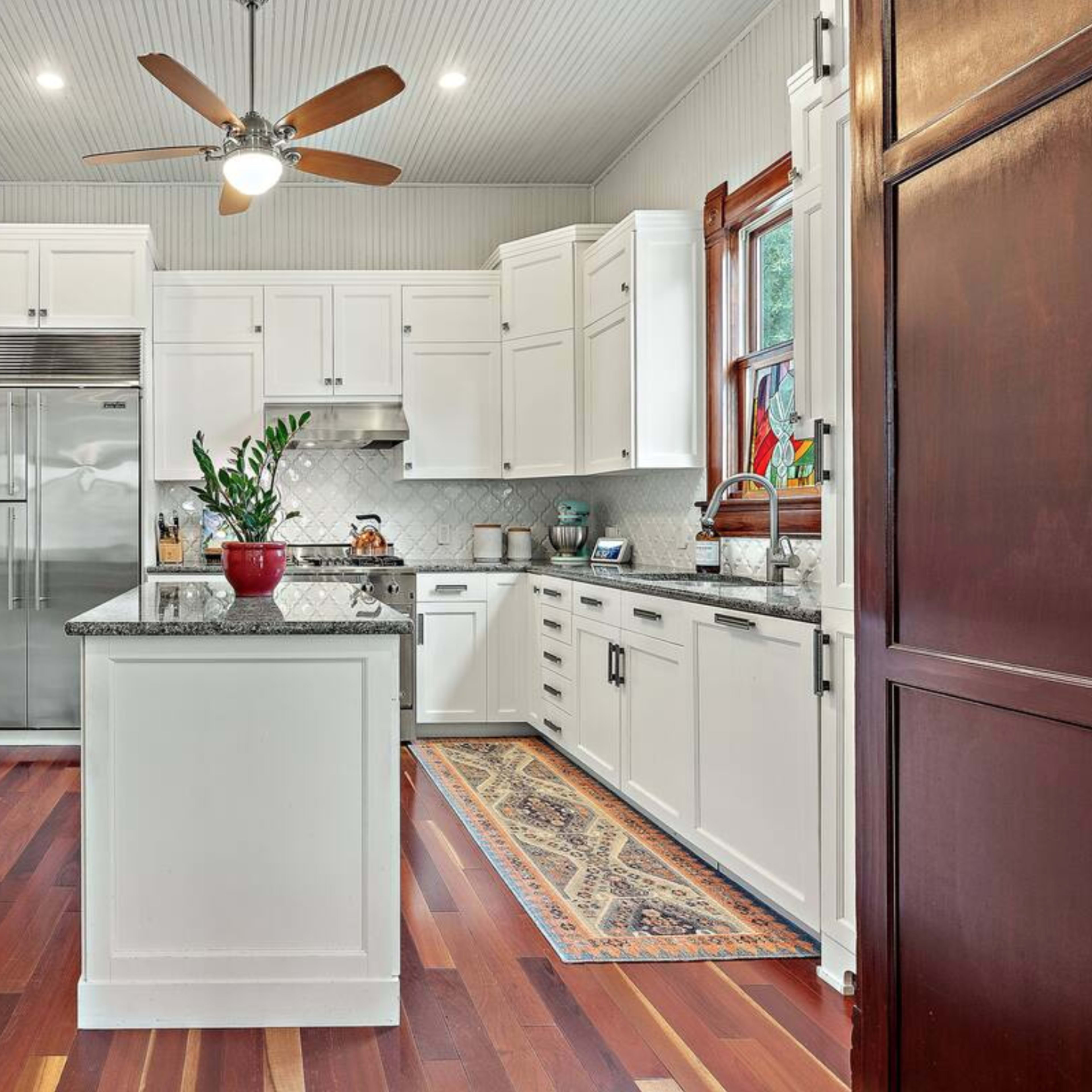 A modern kitchen with white cabinets, a large island with a granite countertop, stainless steel appliances, and polished wooden flooring.