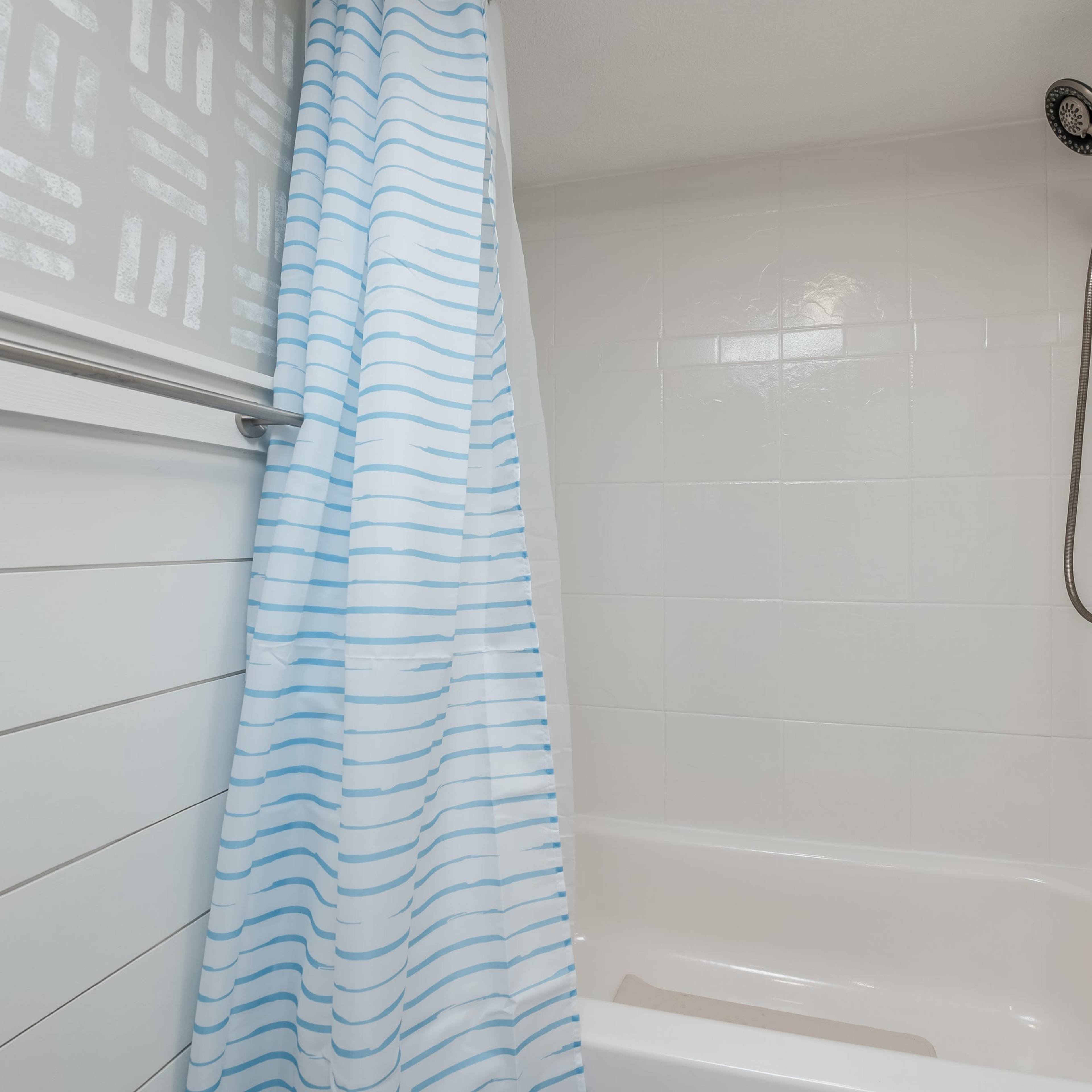 A bathroom features a white bathtub with a blue-striped shower curtain and a handheld showerhead mounted on the wall.