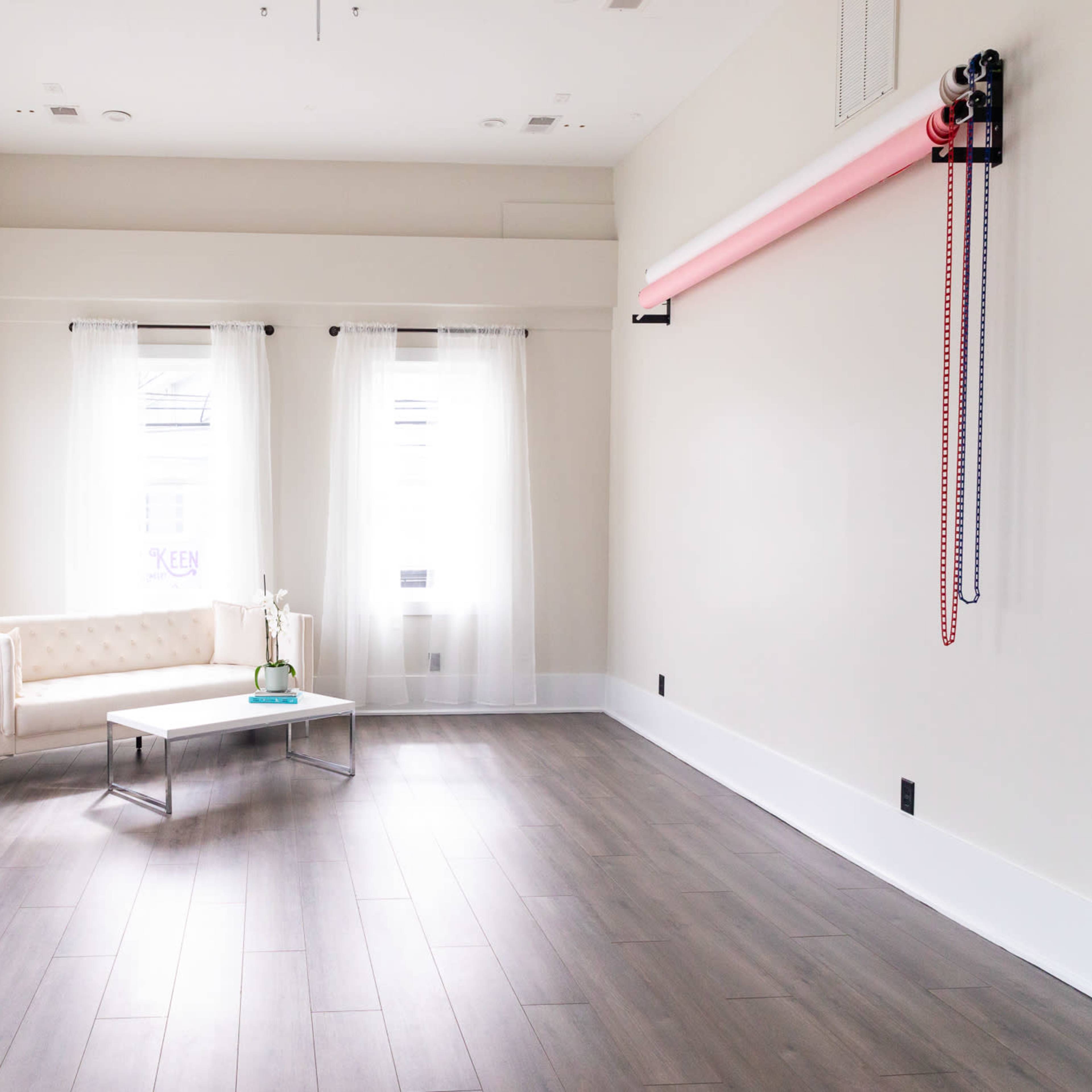 A minimalist room with light wooden floors, a white couch, a coffee table, and large windows with sheer curtains.