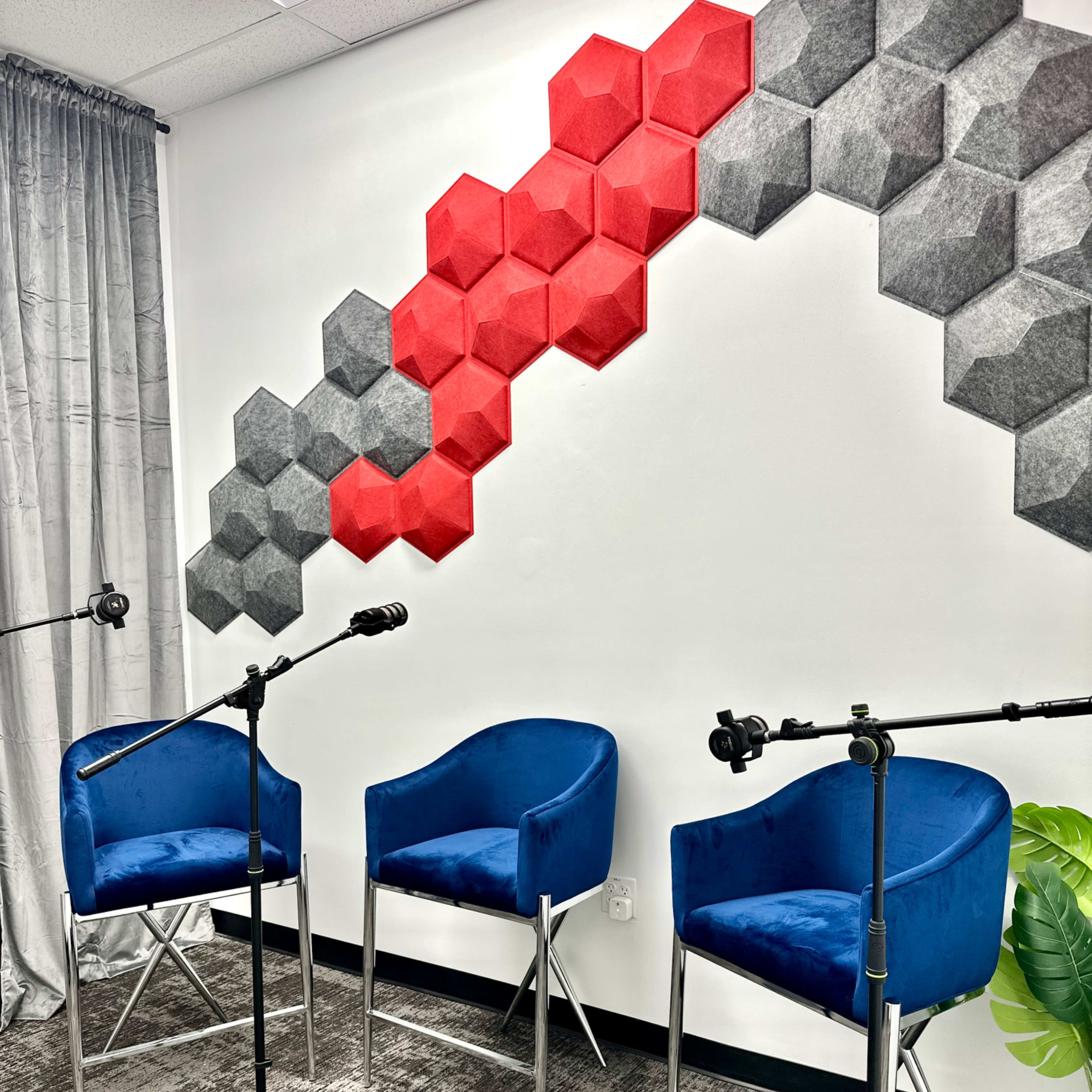 A modern seating area features two blue chairs and microphone stands against a wall adorned with red and gray hexagonal sound panels.