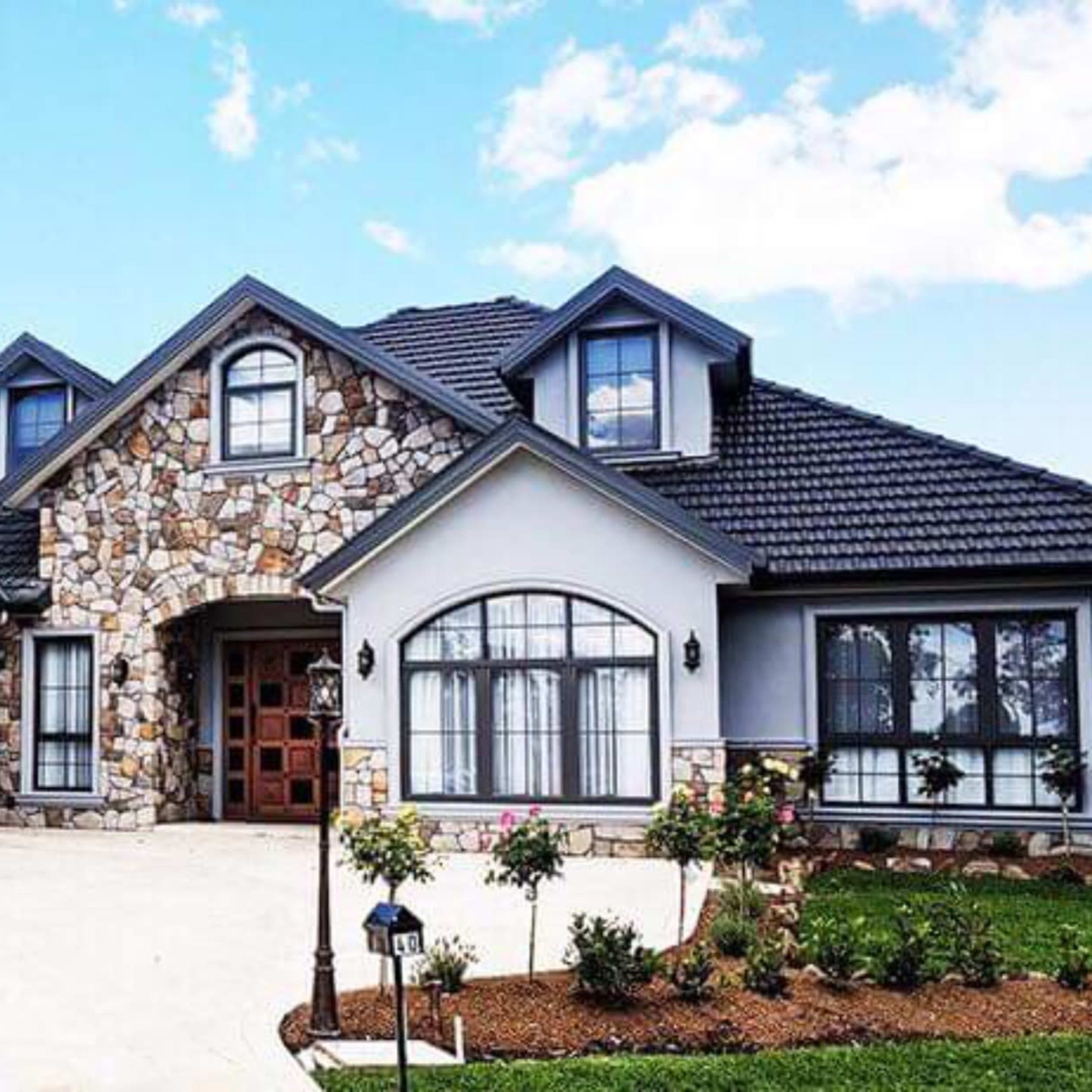 A large, modern house with a stone facade and a two-car garage, set against a clear blue sky.