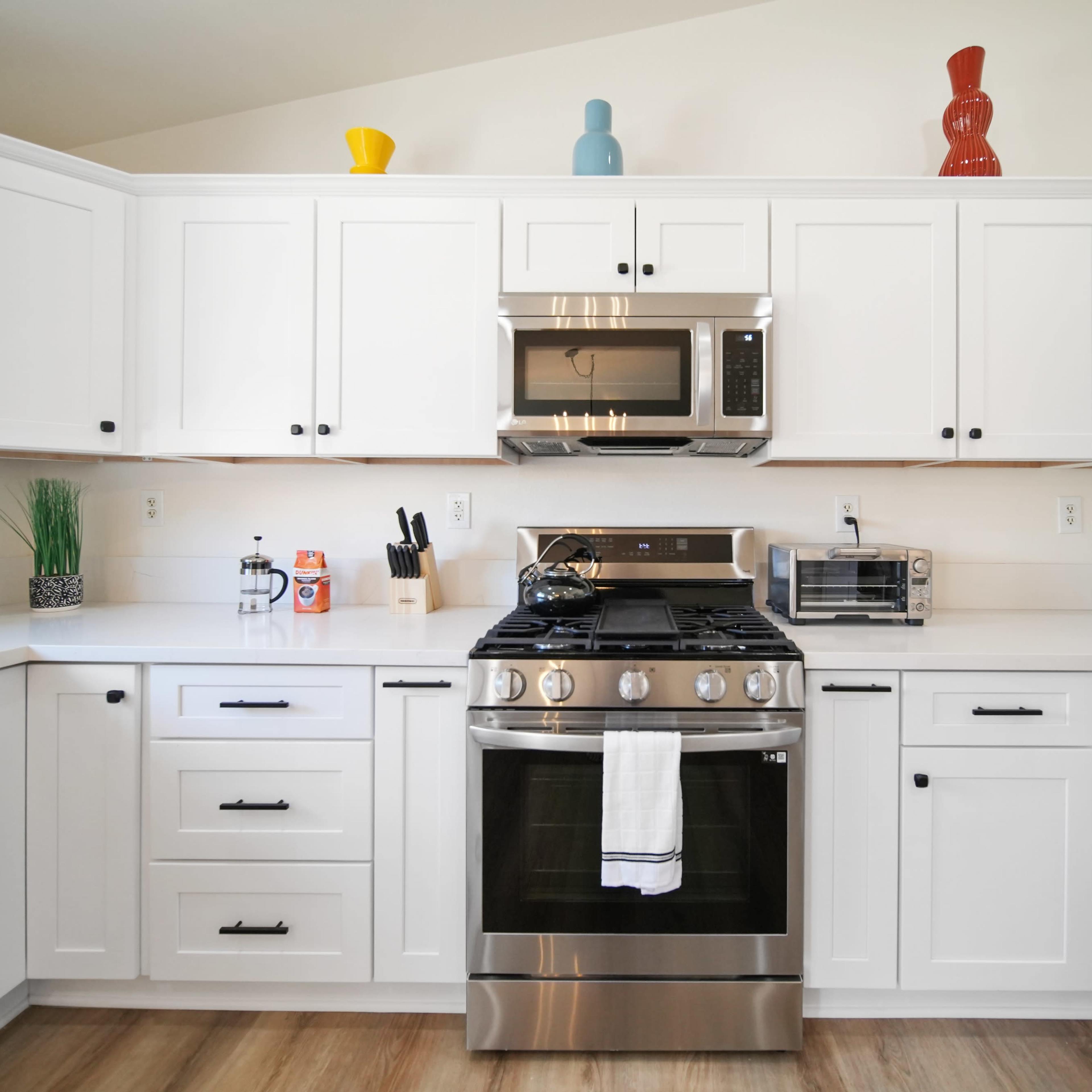 A modern kitchen features white cabinetry, stainless steel appliances, and decorative items on the shelves.