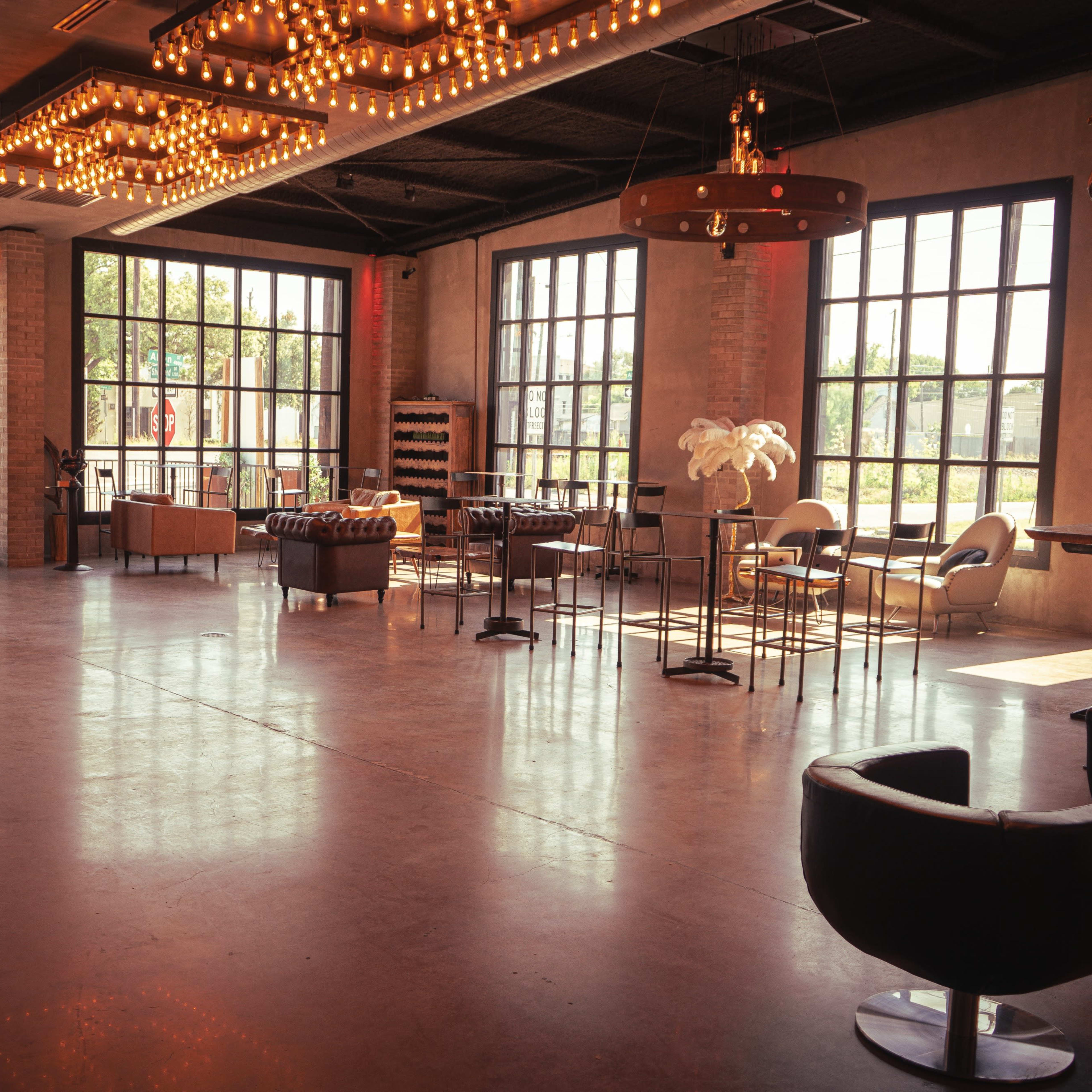 A spacious interior of a well-lit lounge with large windows, featuring modern furniture and decorative lighting fixtures.