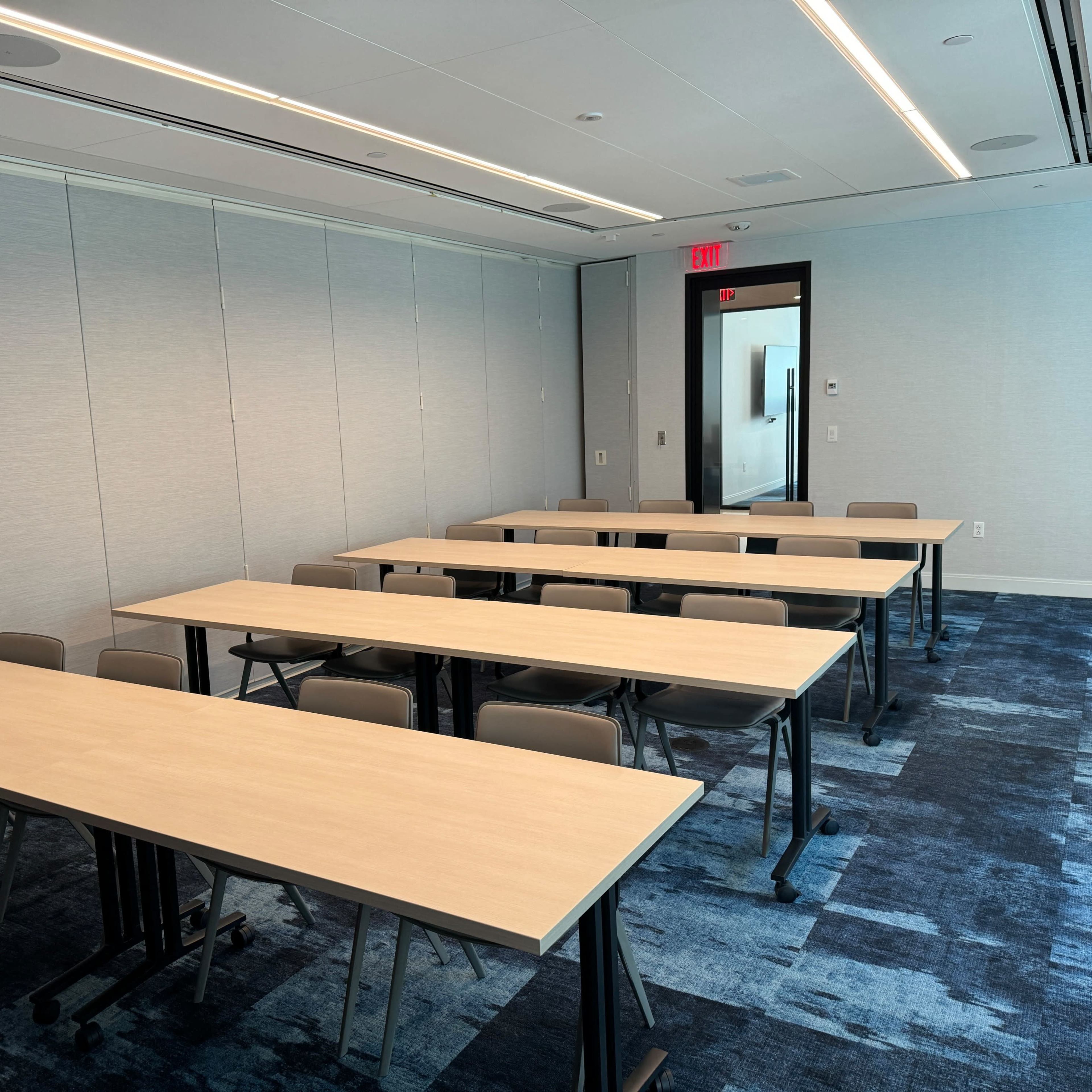 A modern conference room with several tables arranged in rows and a blue carpeted floor.