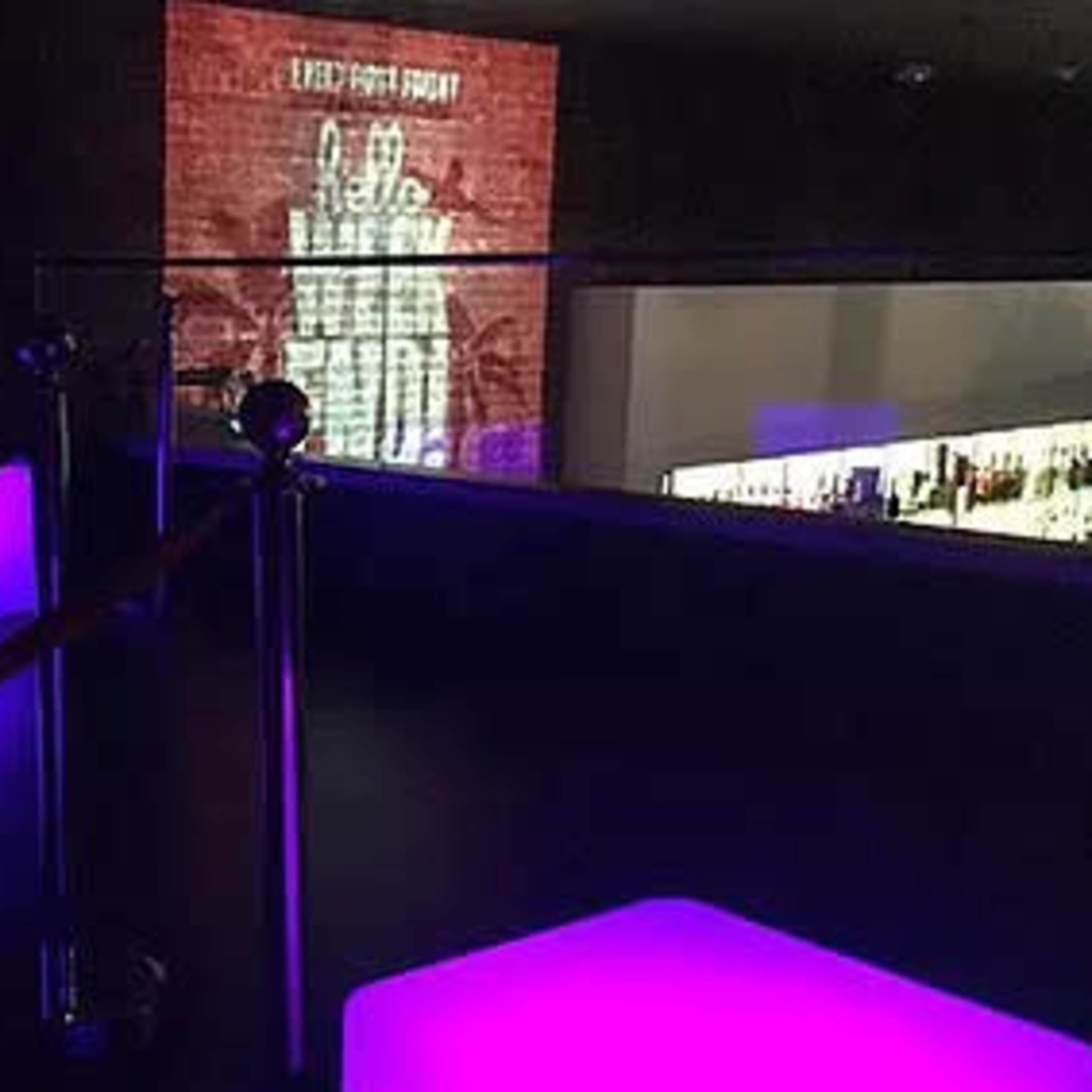 A dimly lit lounge area with glowing purple seating and a large projection on the wall.