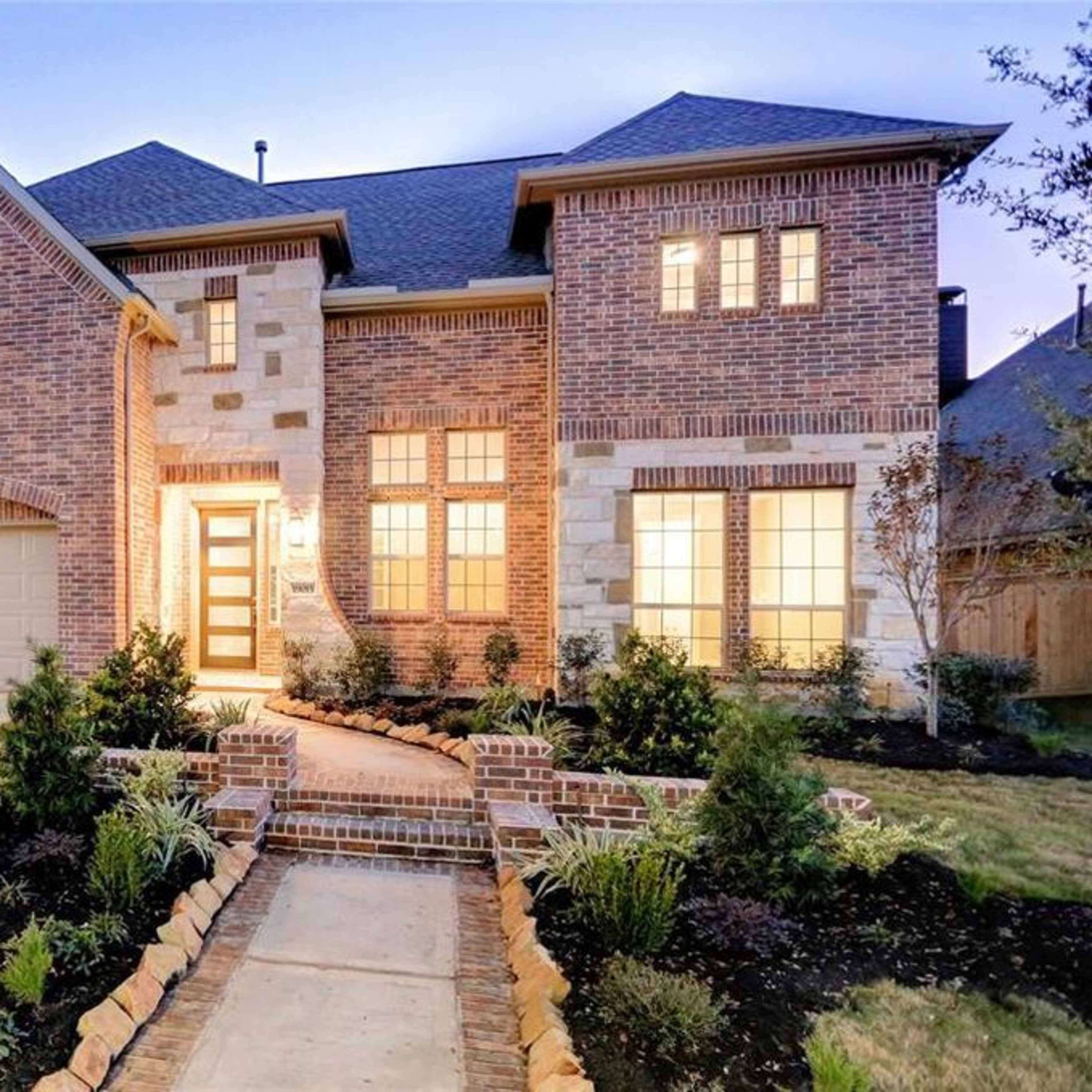 A modern brick house with a well-lit facade, a landscaped front yard, and a driveway leading to a two-car garage.