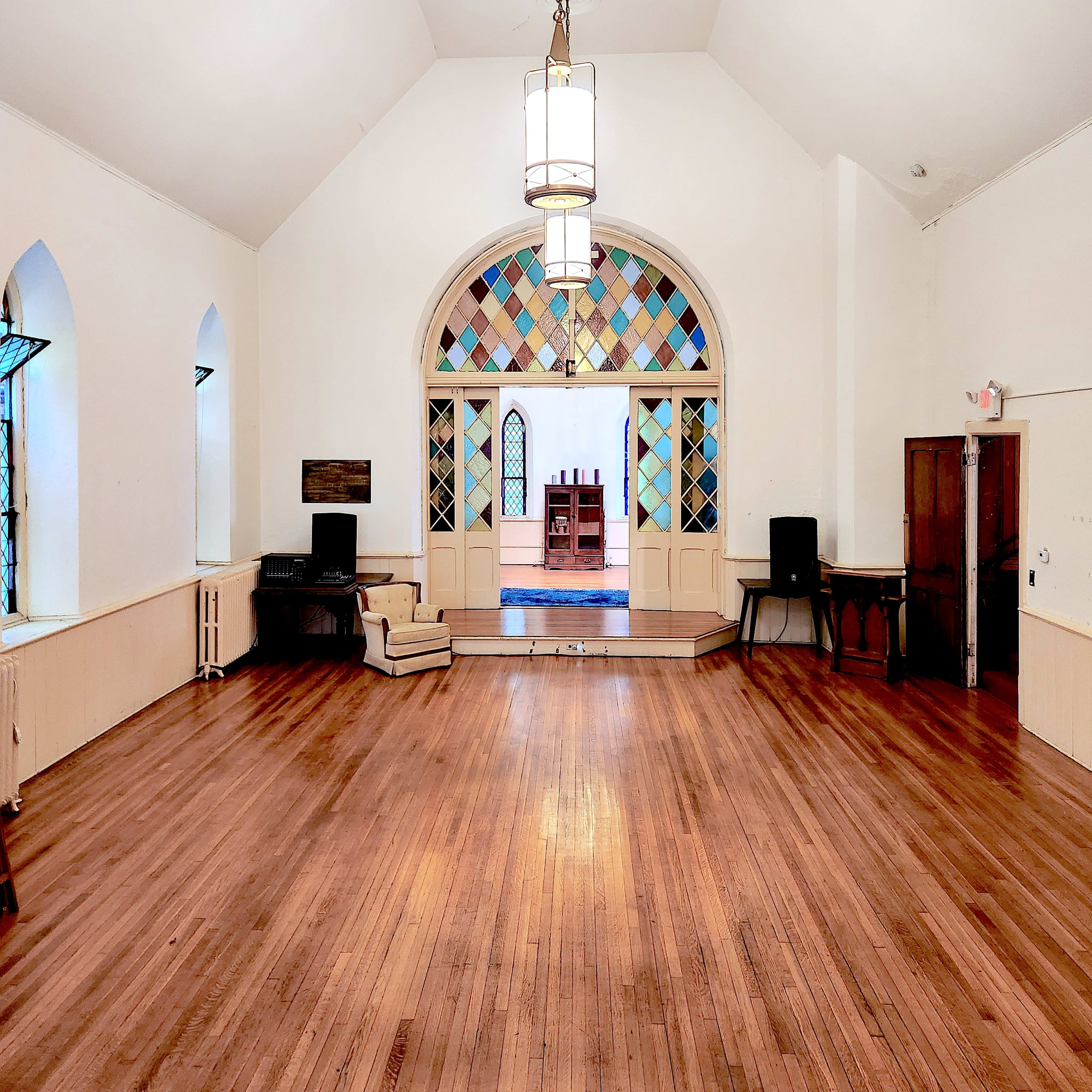 The interior of a spacious, well-lit room features hardwood floors and large arched windows with colorful panes.