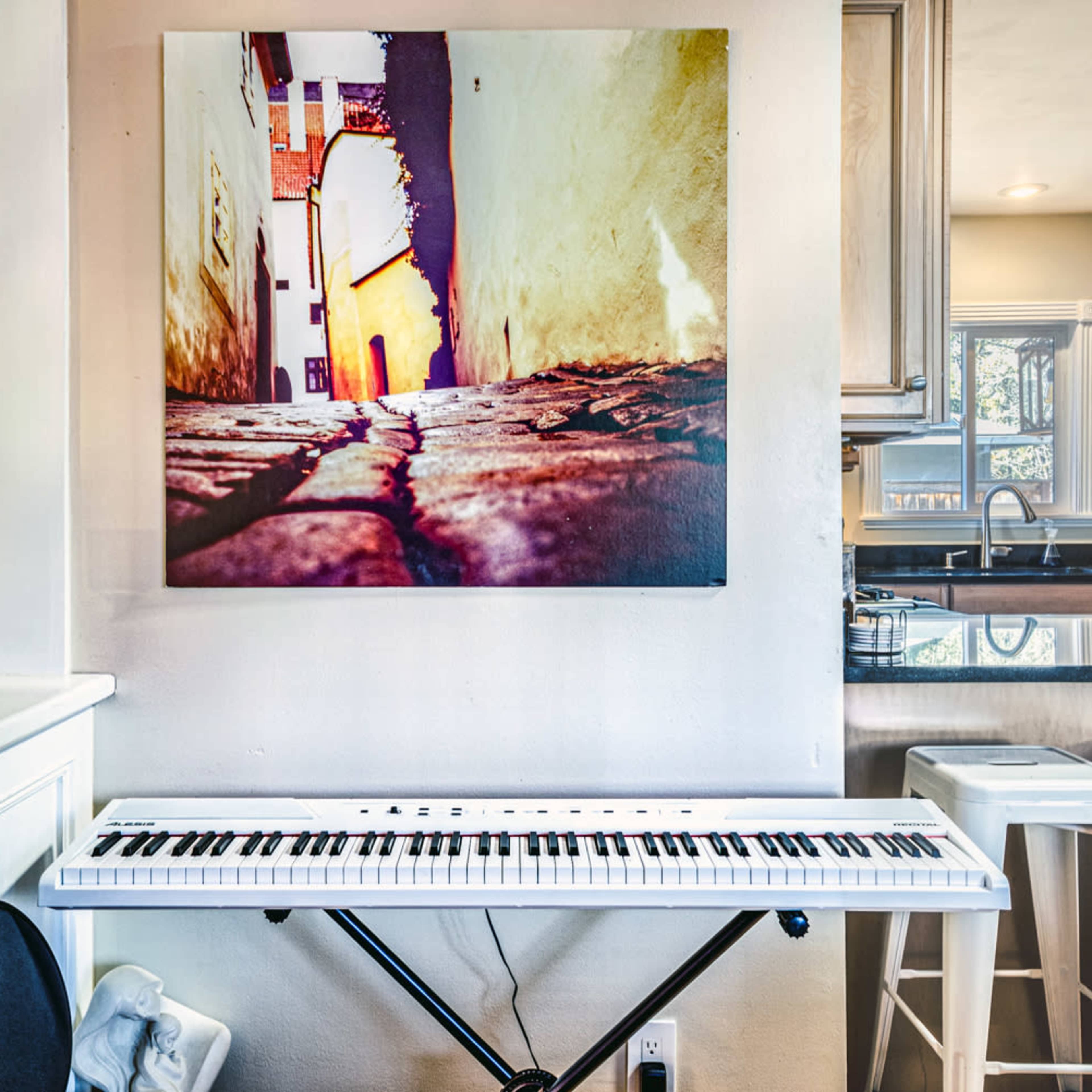 A white keyboard is positioned beneath a colorful photograph of a narrow alleyway, displayed on the wall beside a kitchen bar area.