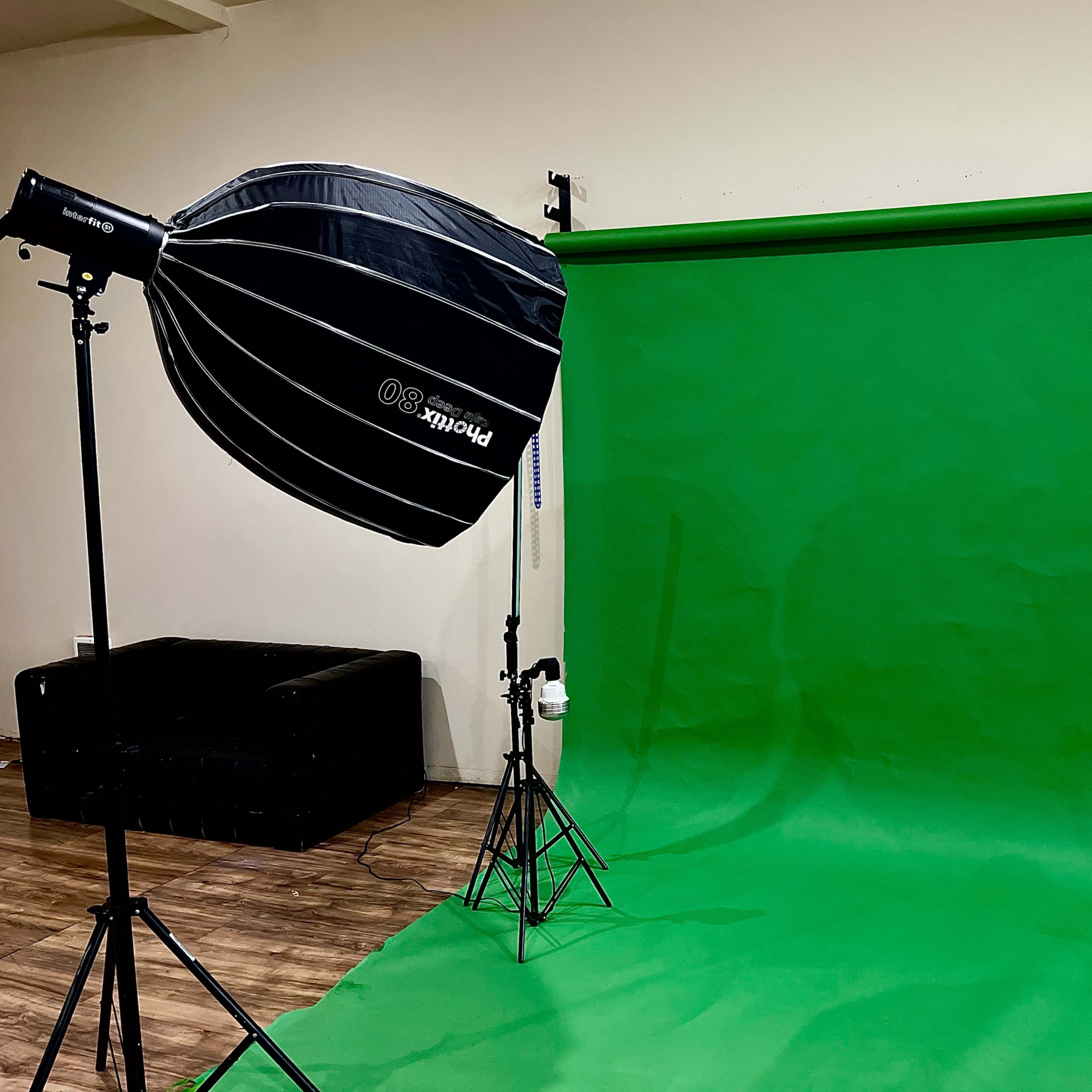 A photography studio setup featuring a green backdrop, a softbox light on the left, and a strobe light on the right.