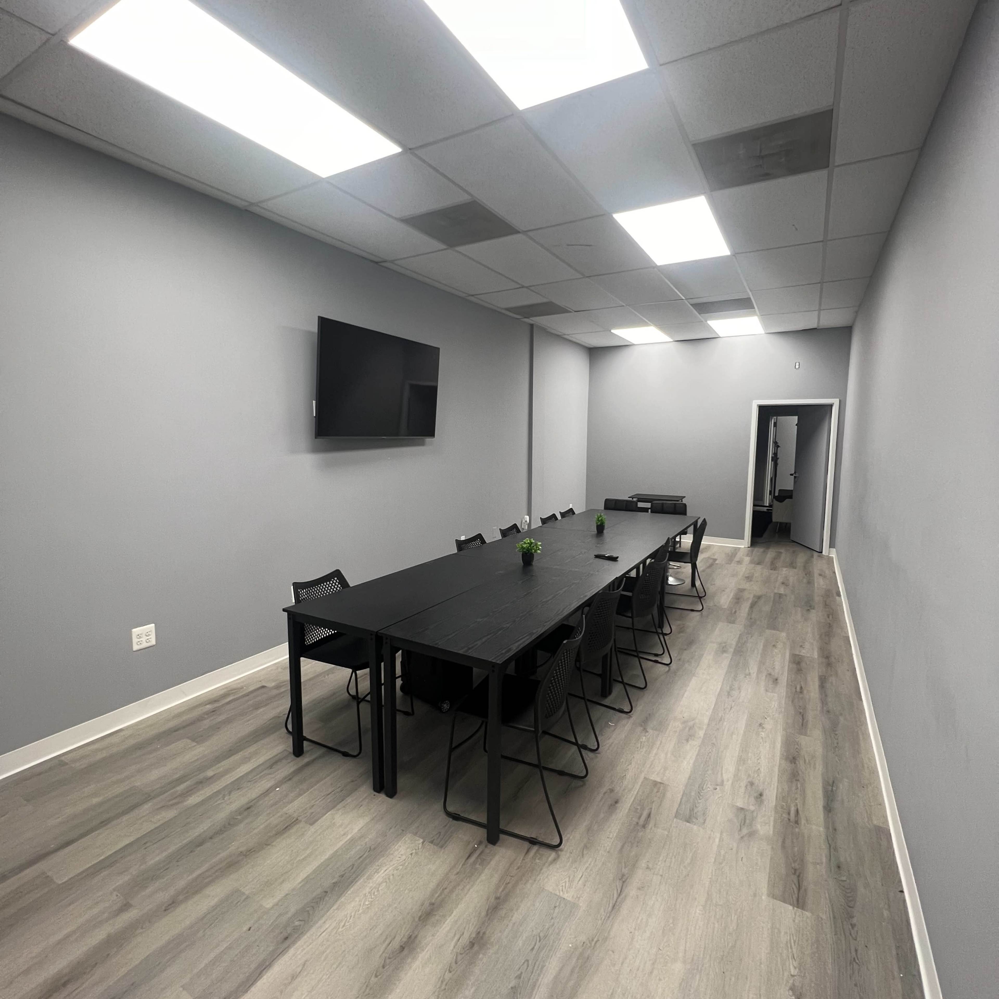 A large conference room with a long black table surrounded by chairs, illuminated by bright ceiling lights.