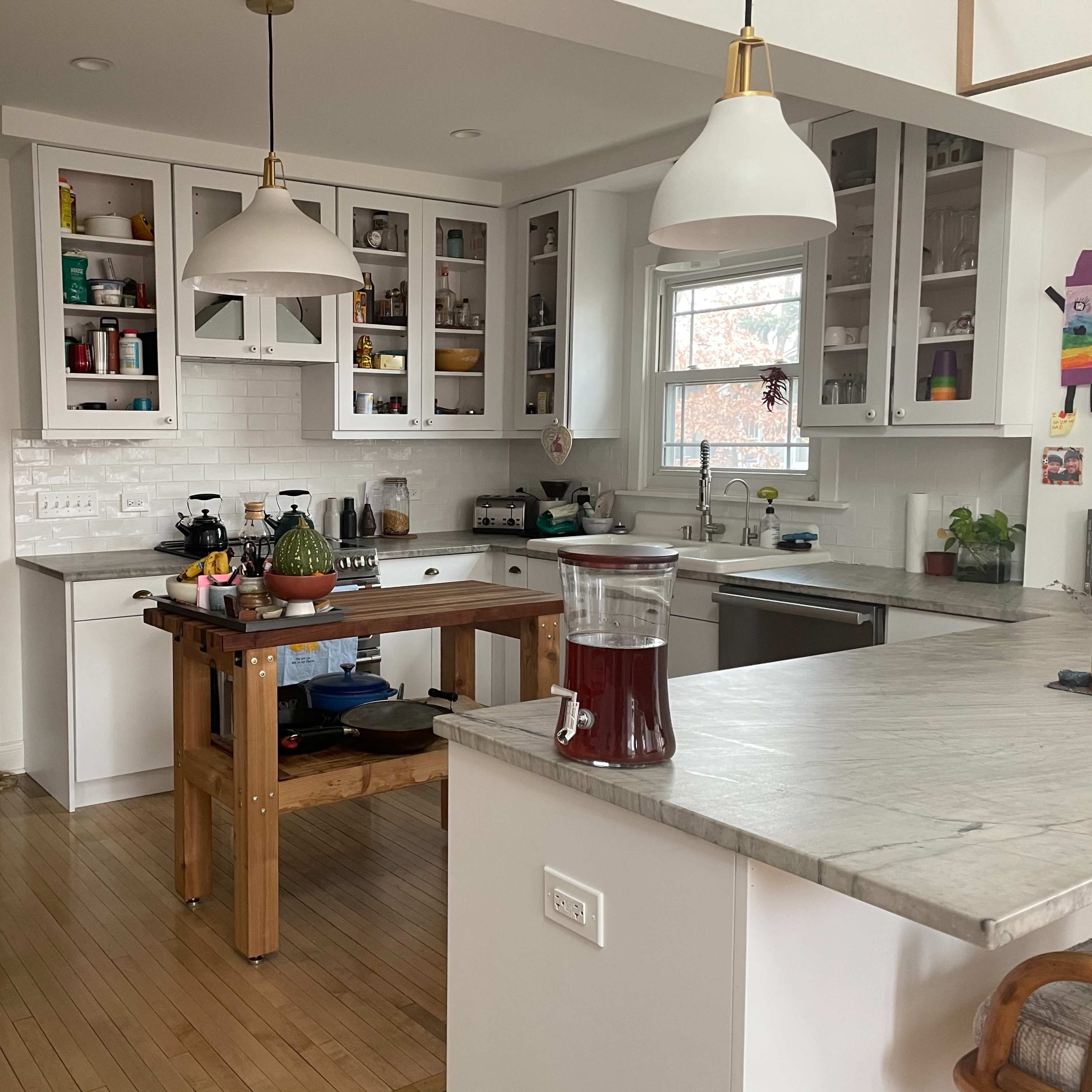 A modern kitchen features a central wooden island, white cabinetry, and natural light coming through a window.