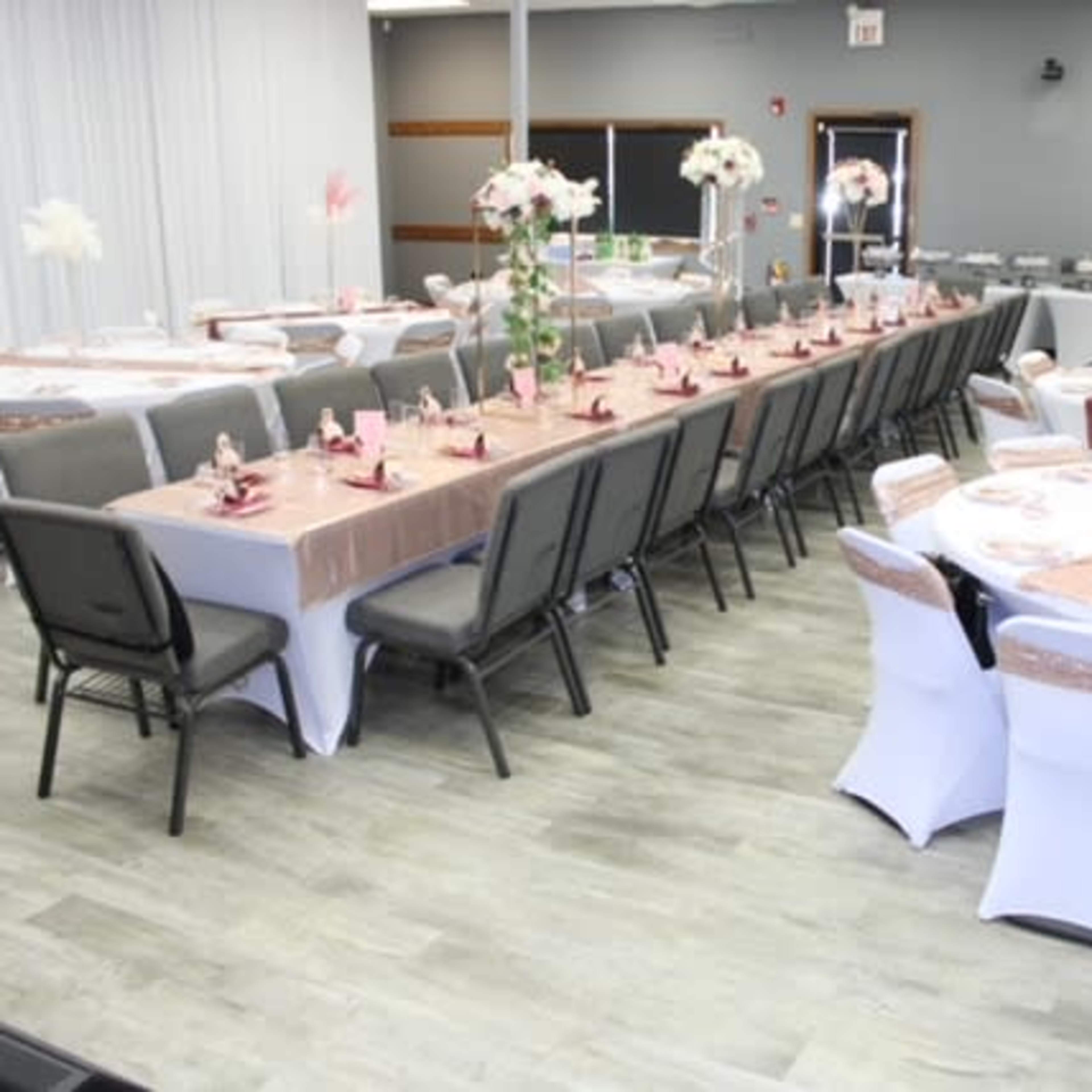 A large event space is set with neatly arranged tables covered in white linens and adorned with floral centerpieces.