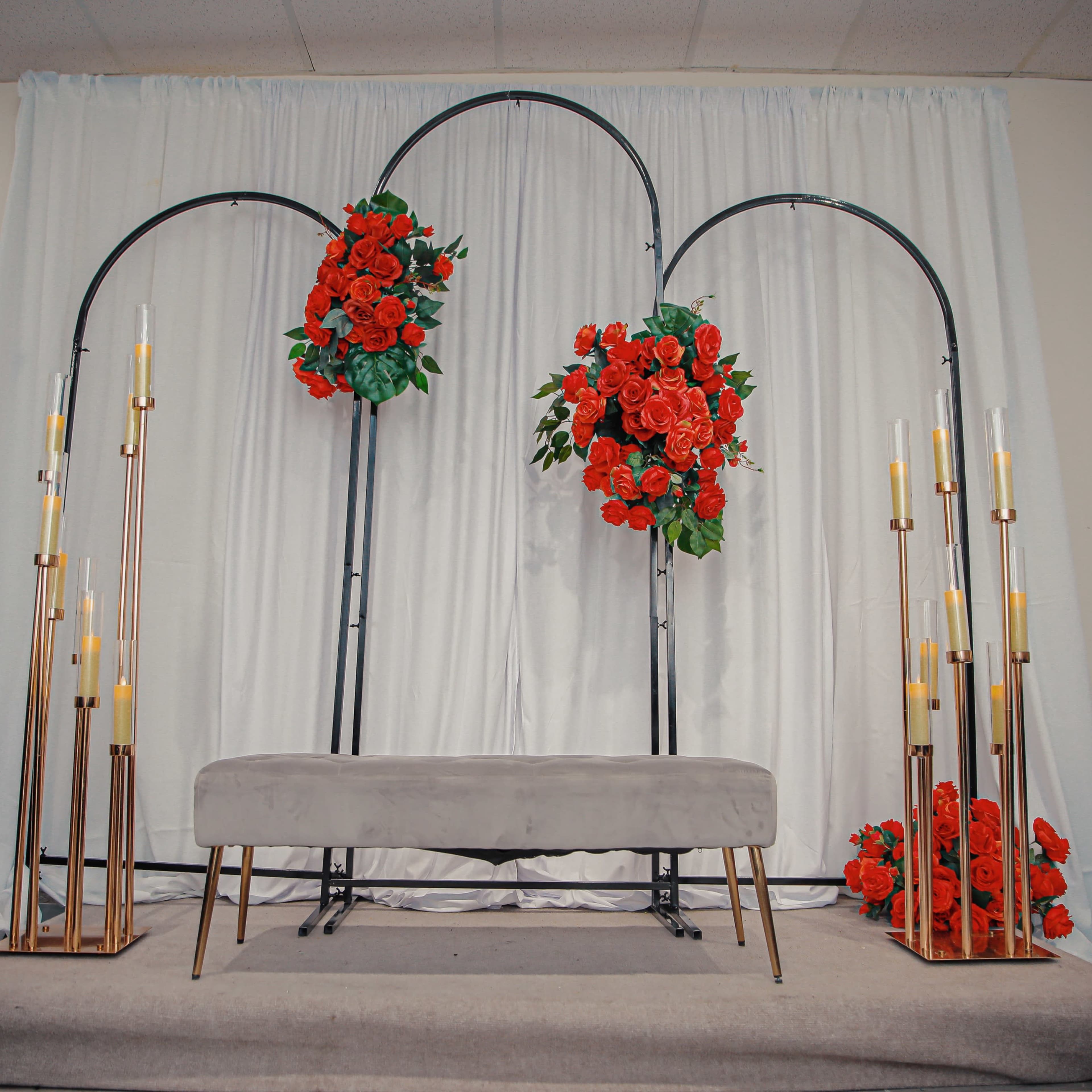 A floral archway with red flowers is set up against a white backdrop, flanked by tall gold candleholders.