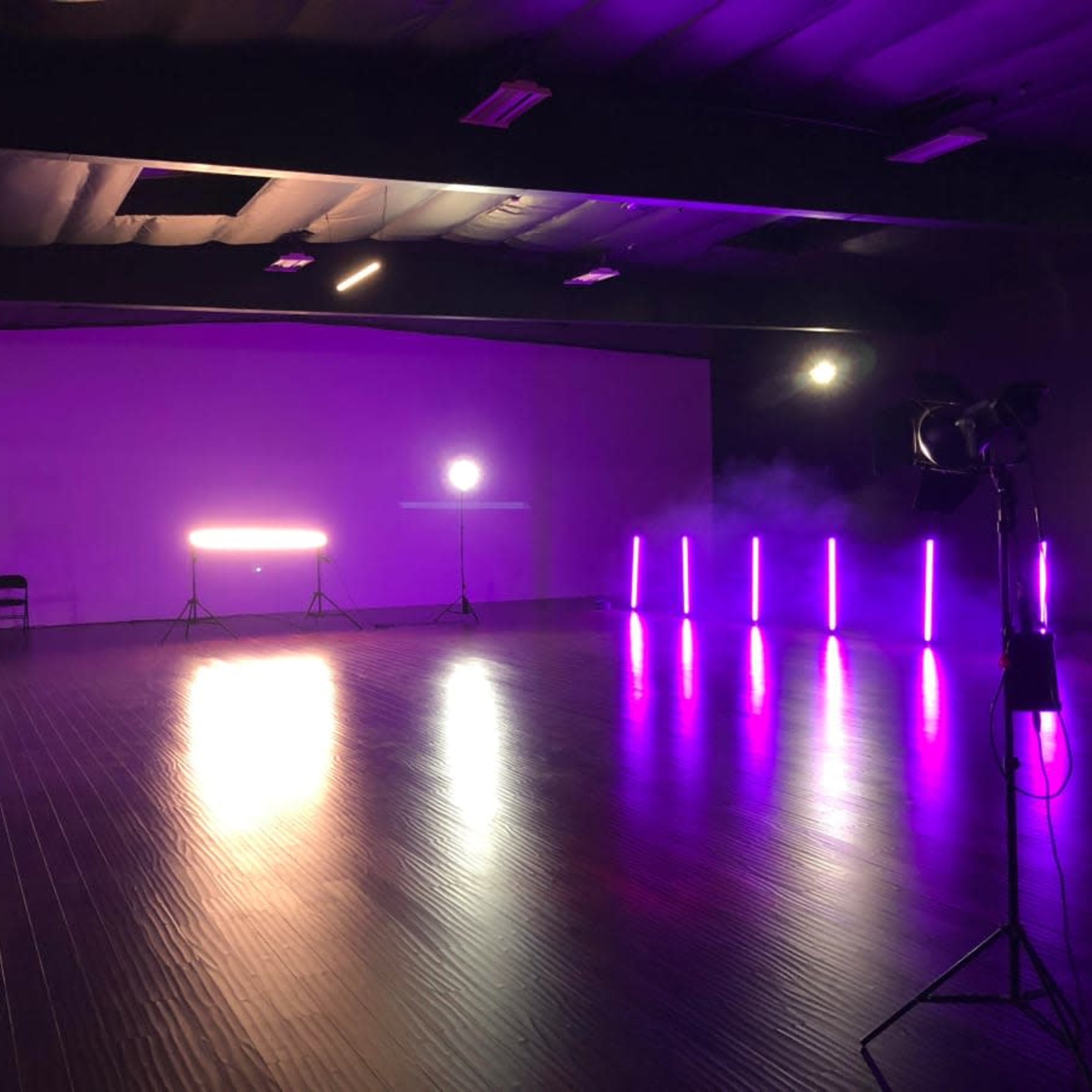 A spacious studio is illuminated by purple lighting and equipped with audio speakers and multiple light stands.