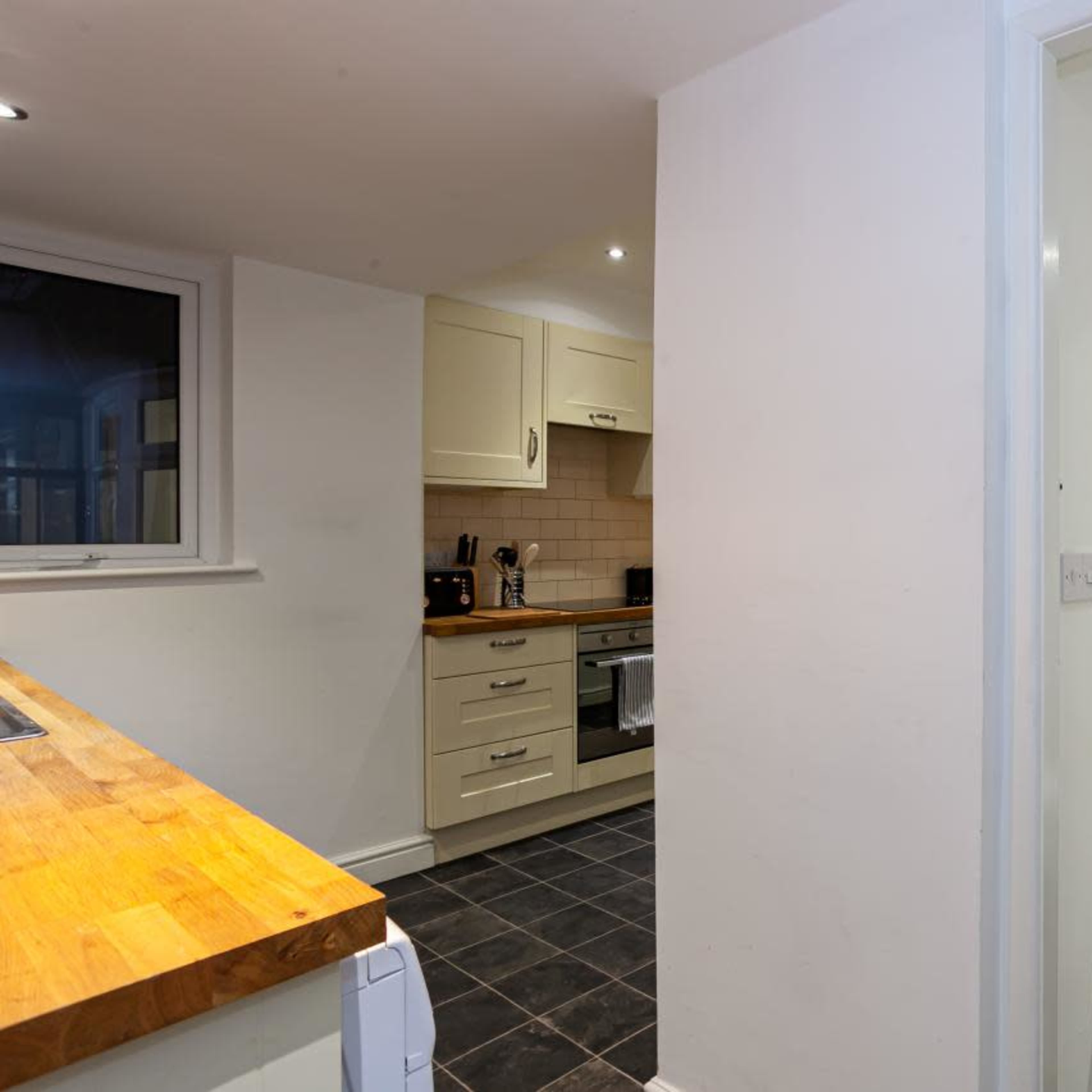 A modern kitchen with light cabinetry and a small adjacent bathroom featuring a toilet and sink.