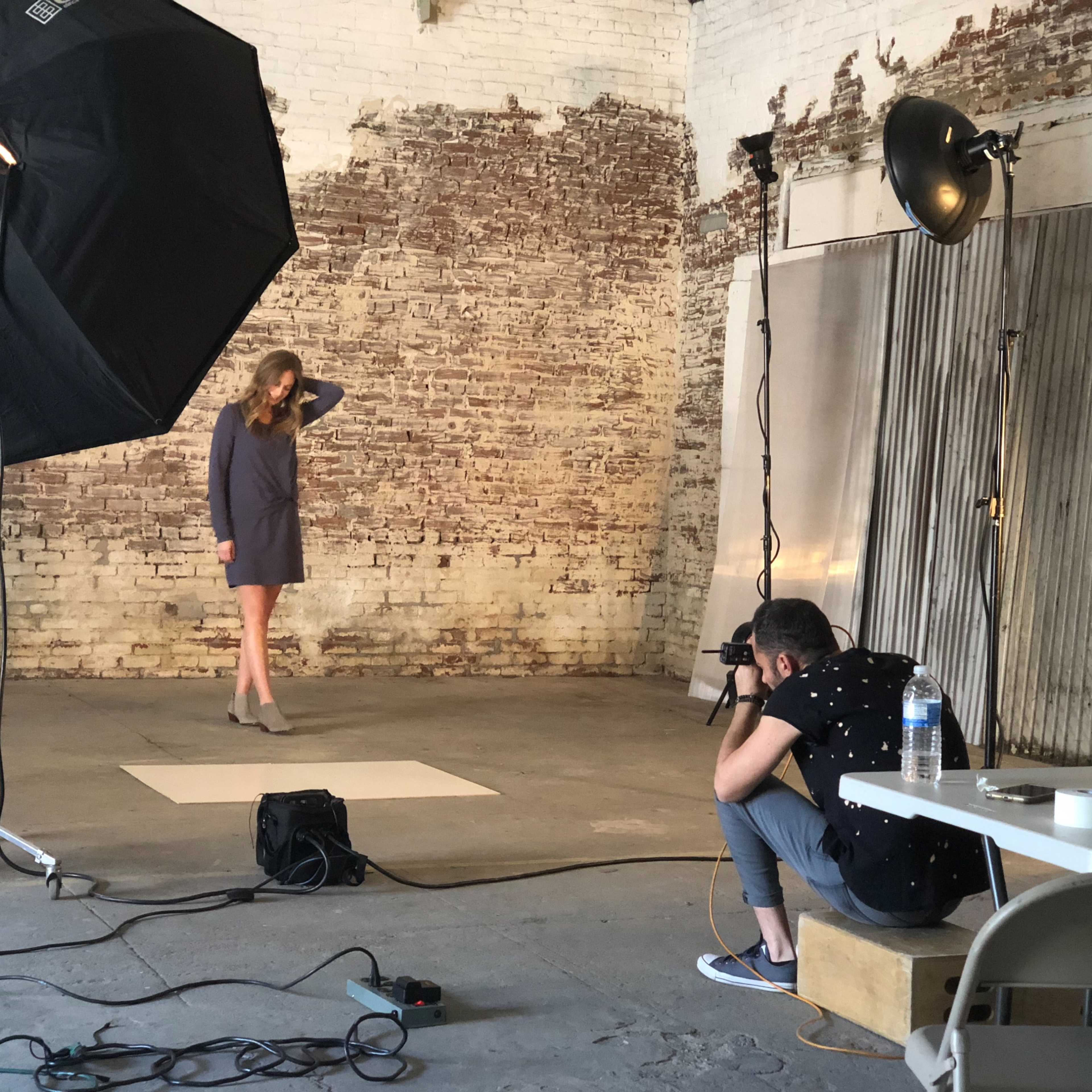 A model poses in an industrial studio while a photographer captures images from a crouched position.