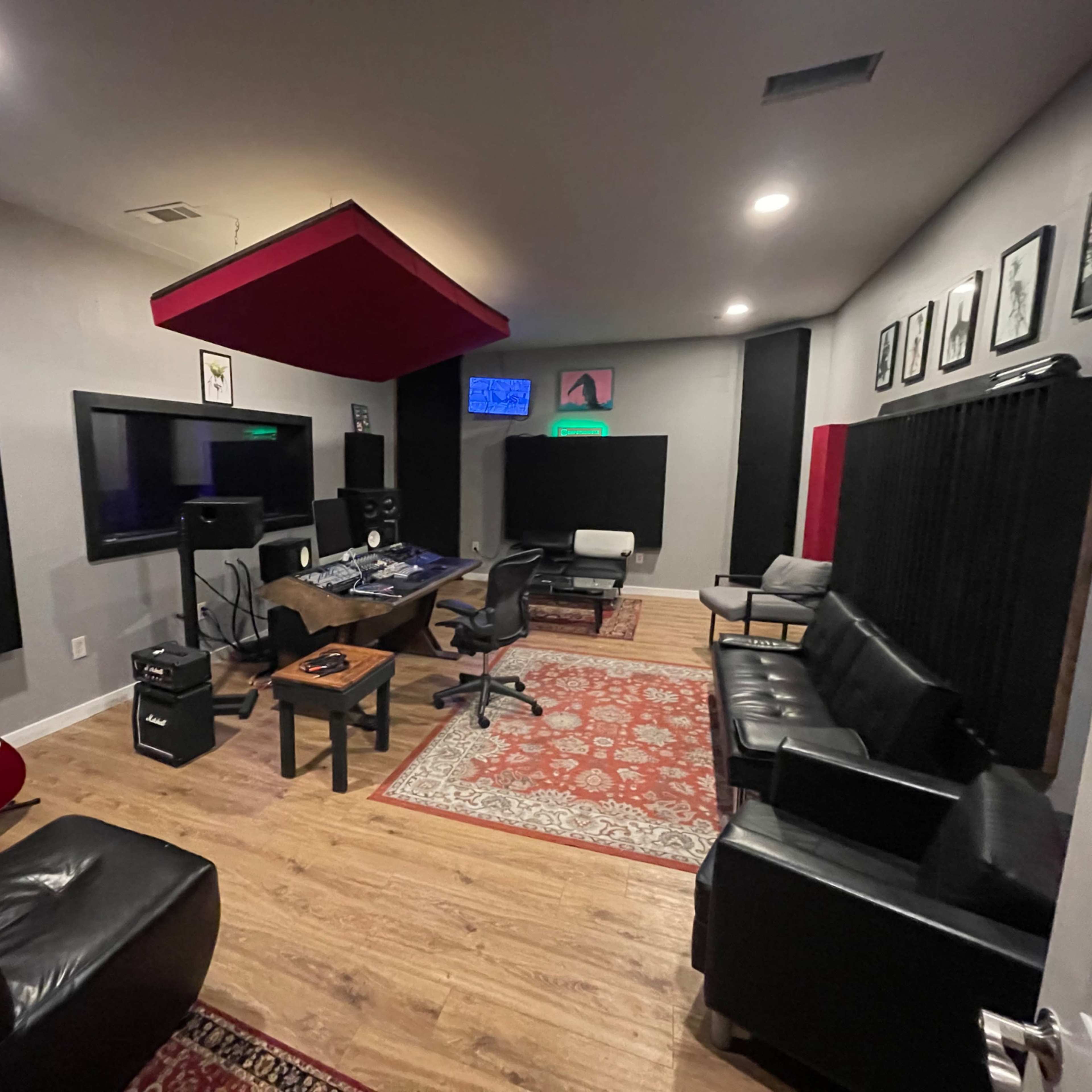 A modern music recording studio with guitars, soundproofing panels, and a control desk surrounded by seating.