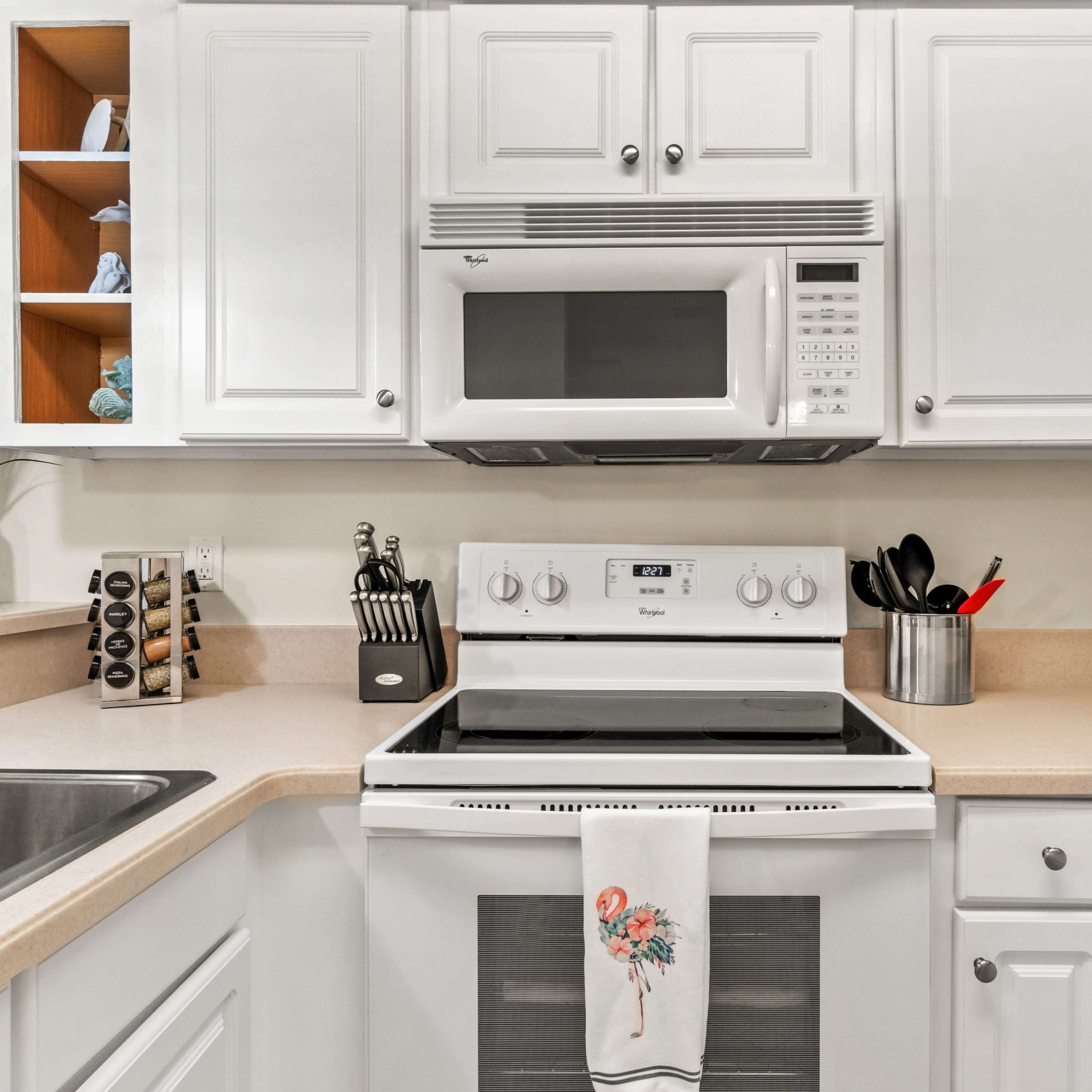 A modern kitchen with white cabinetry, a stove, a microwave, and various kitchen utensils neatly arranged on the countertops.