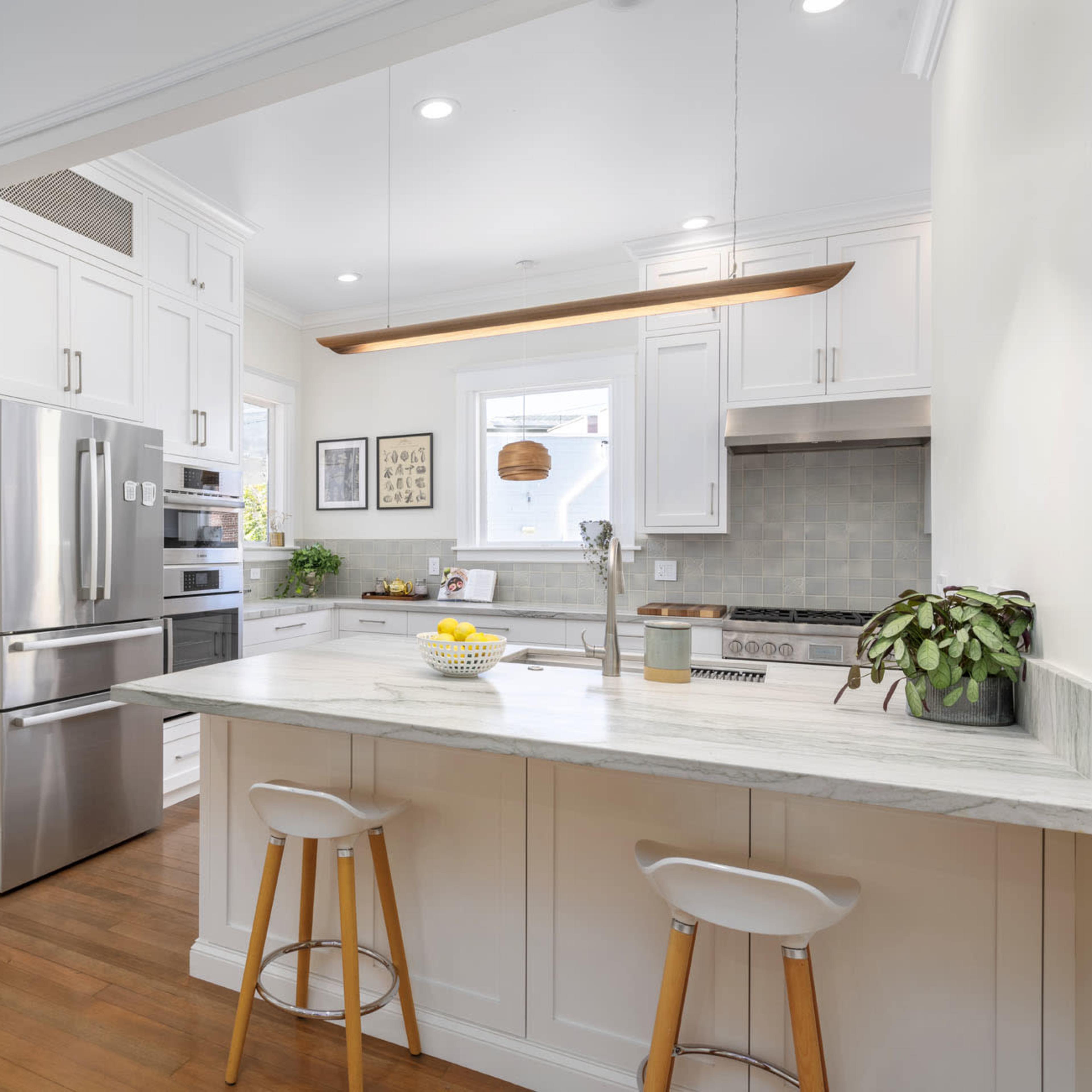 A modern kitchen features white cabinetry, stainless steel appliances, and a central island with bar stools, set against warm wooden flooring.