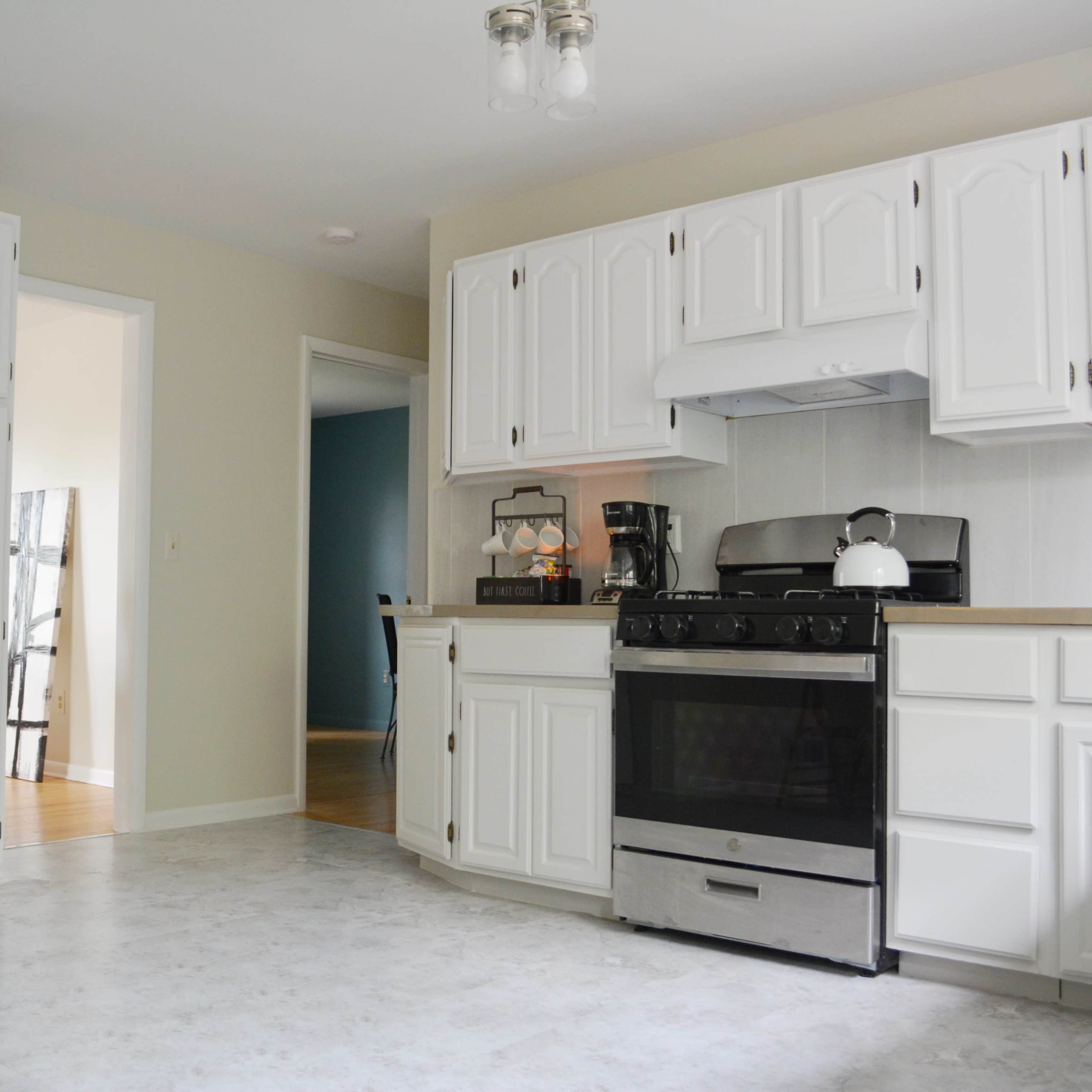 A kitchen features white cabinetry, a gas stove, and a view into an adjoining room.
