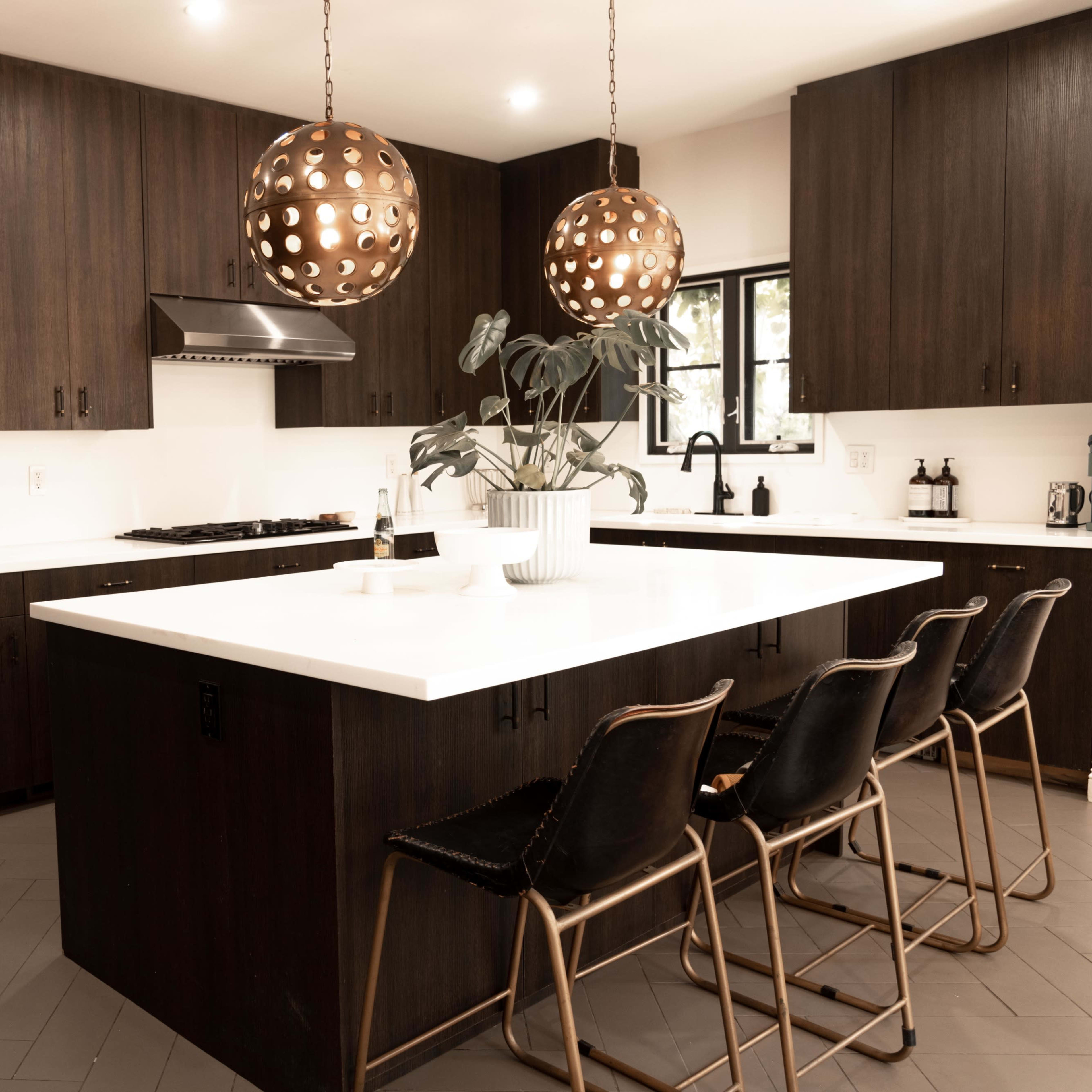 A modern kitchen features a large white island with brown bar stools and pendant lights hanging overhead.