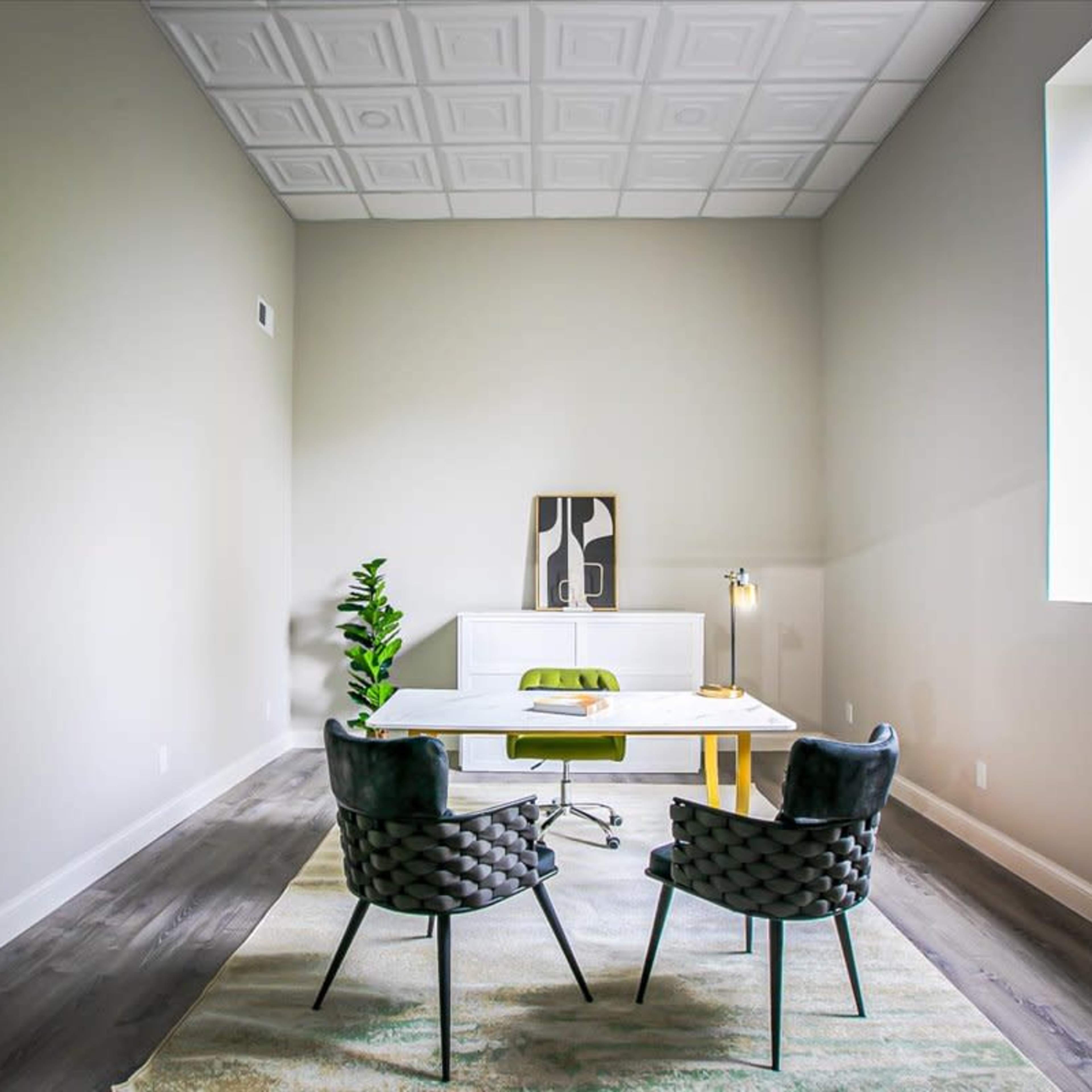 A minimalist office space featuring a white desk, two textured chairs, a floor lamp, and a potted plant, with light-colored walls and a large window.