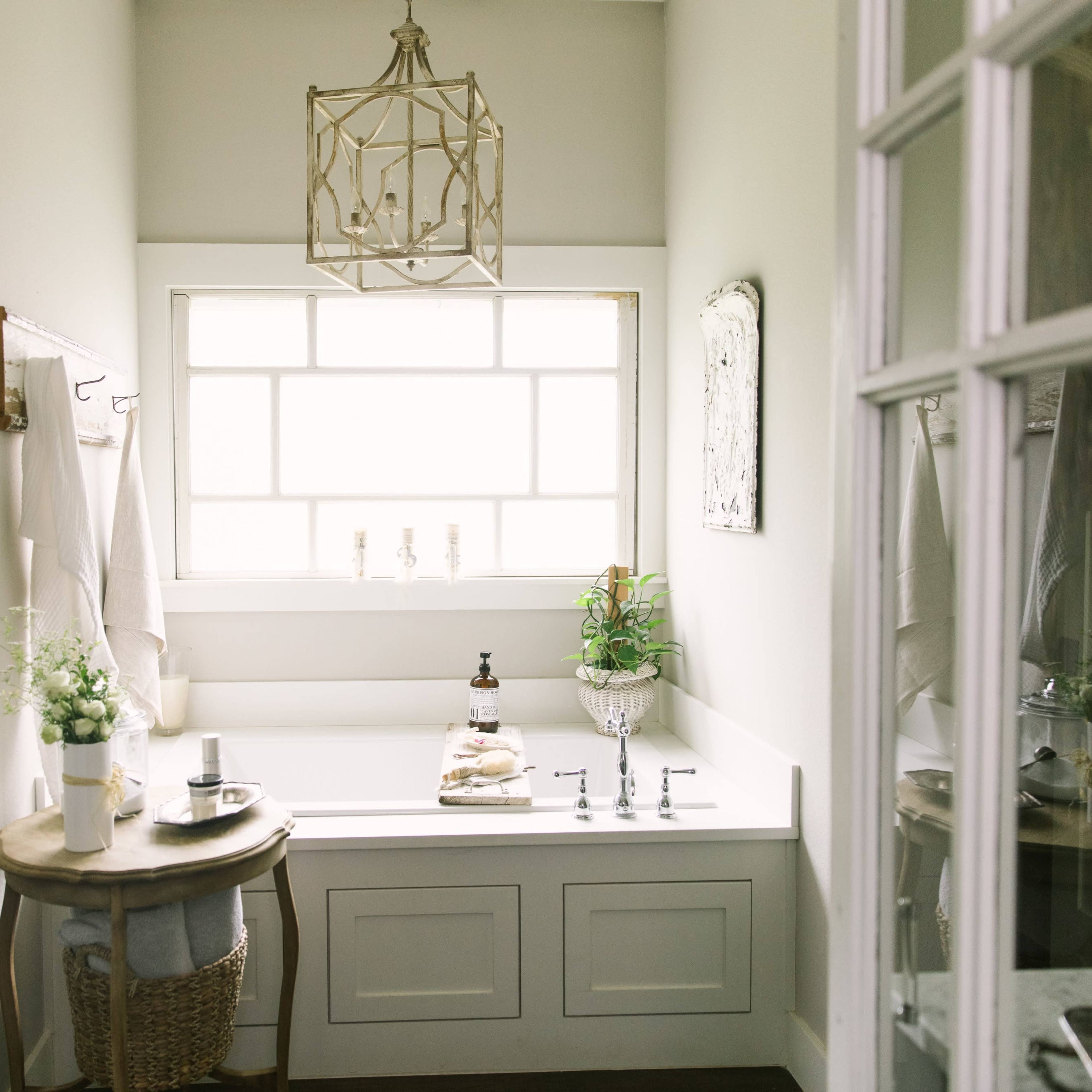A bright bathroom features a large soaking tub beside a window, with decorative accents and a small table displaying toiletries.