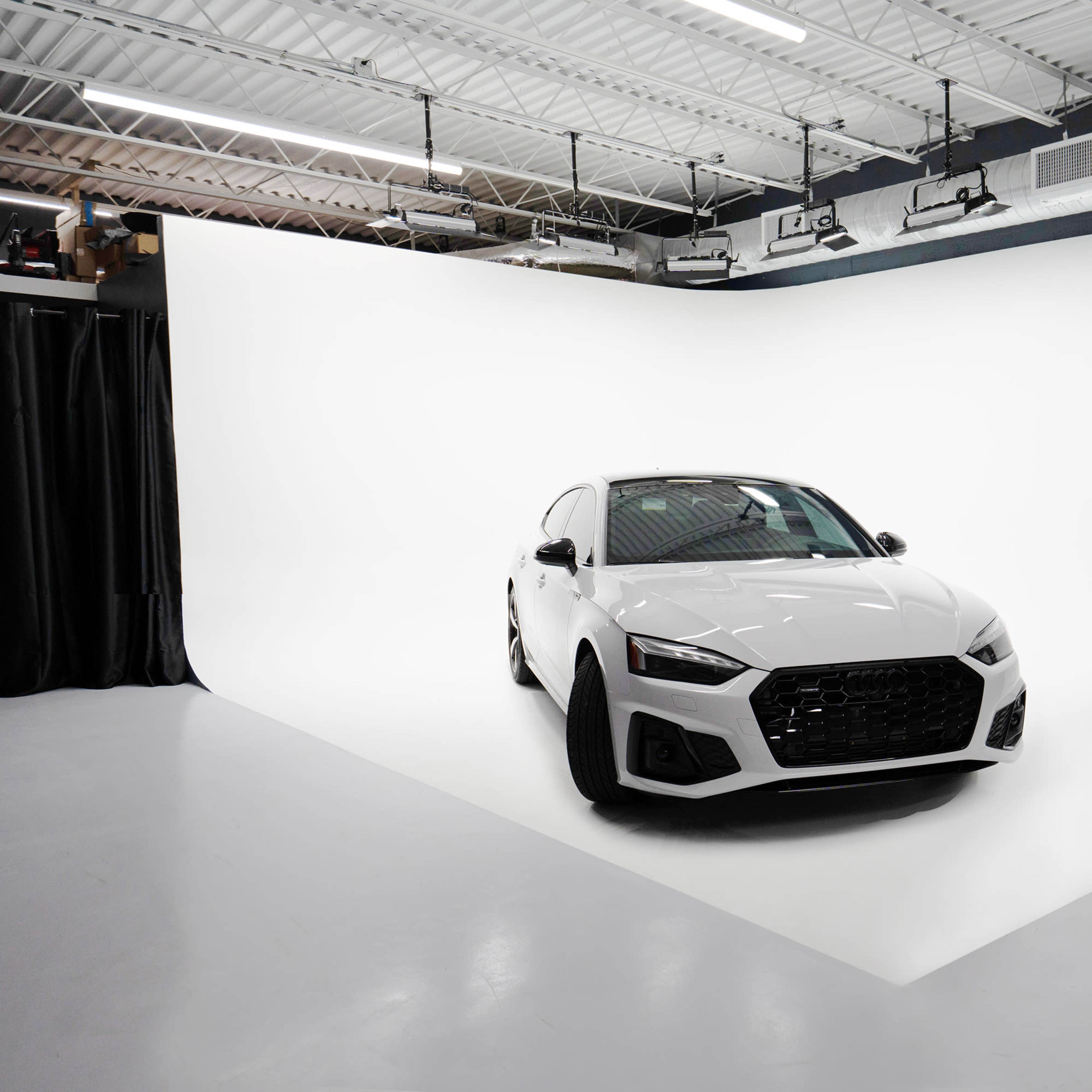 A white sedan is parked on a seamless white backdrop in a photography studio.