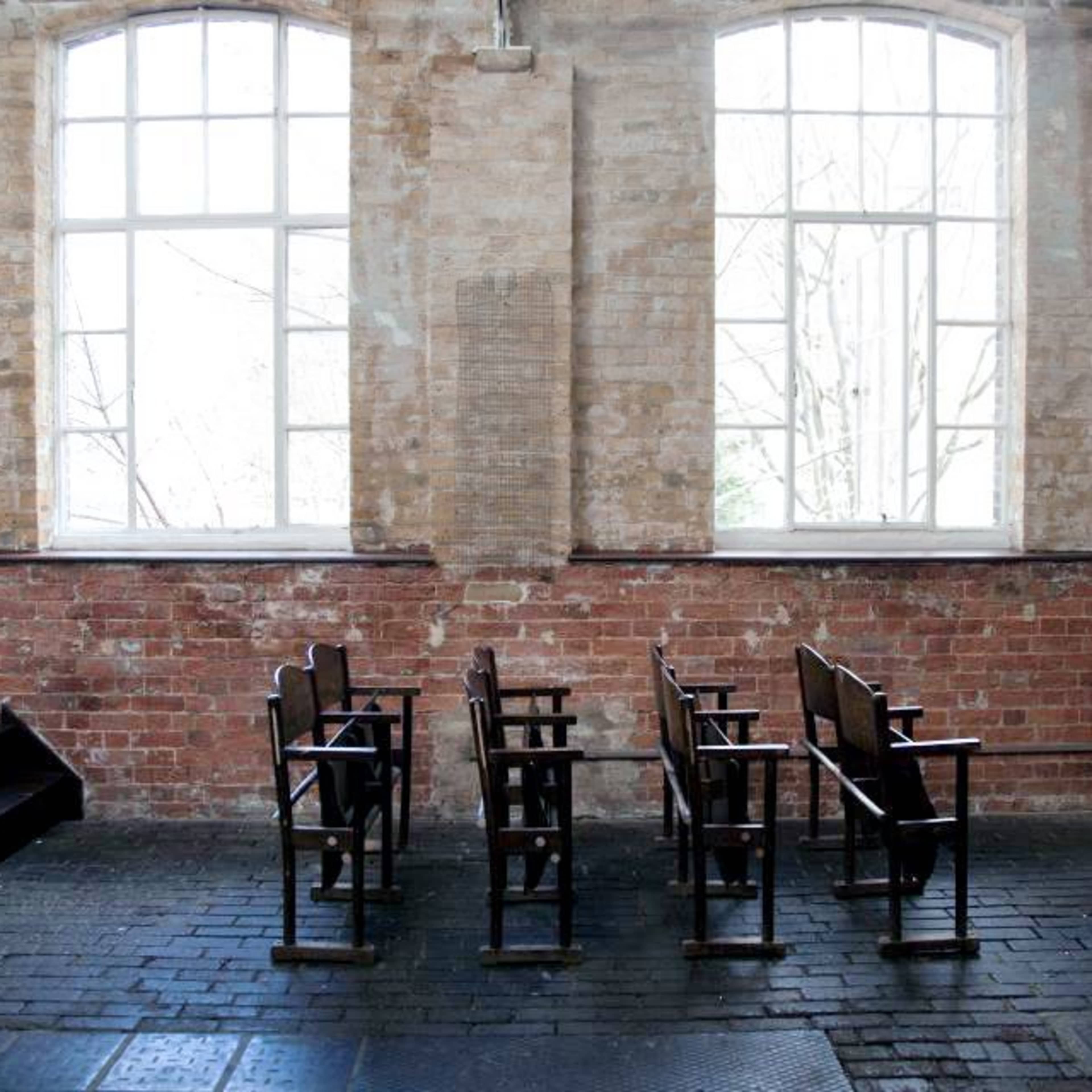 An industrial-style room with exposed brick walls, wooden ladders, a spotlight, a black chair, two wooden stools, and a vintage pommel horse.