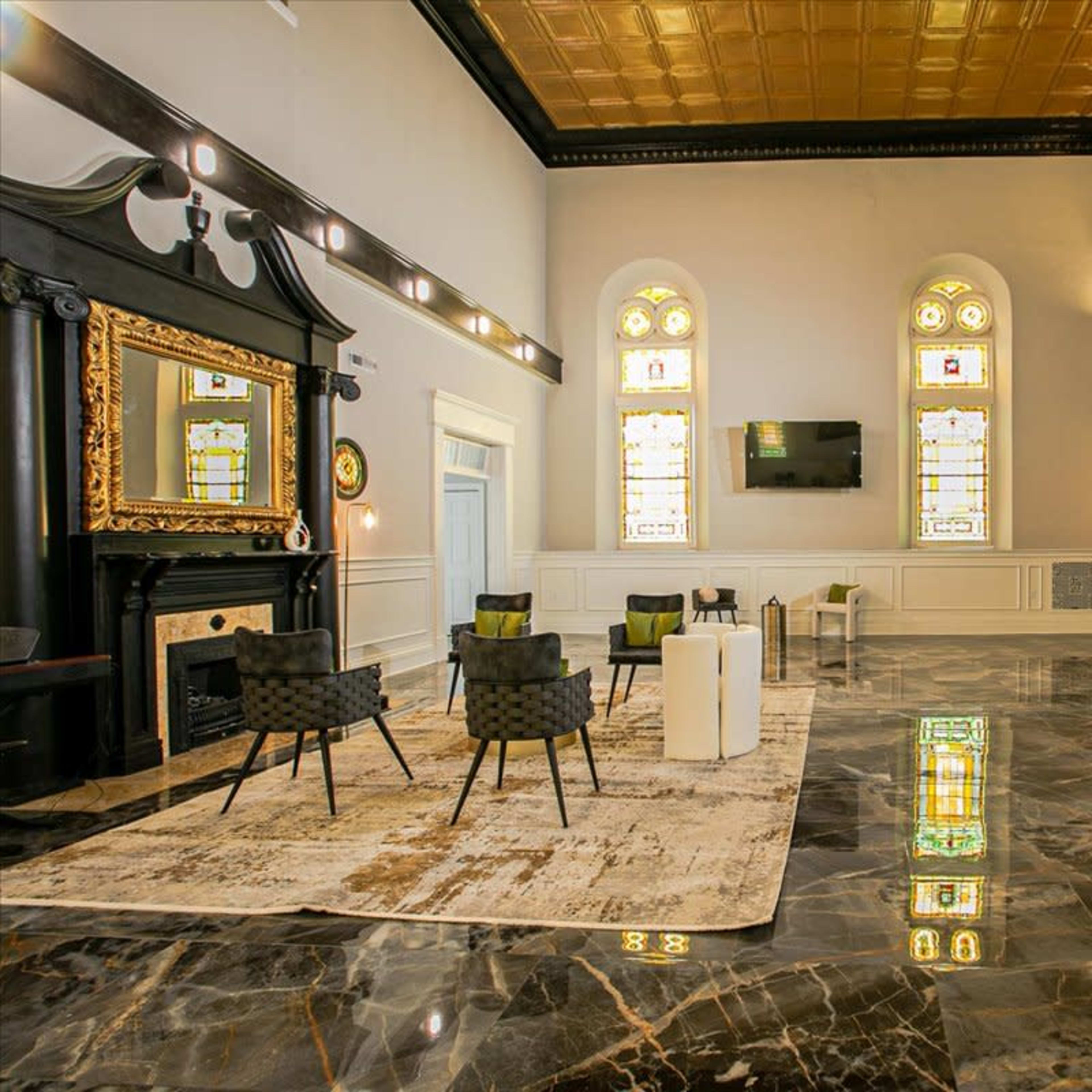 The interior features a spacious room with polished marble floors, large stained glass windows, and elegant furnishings including chairs and a coffee table.