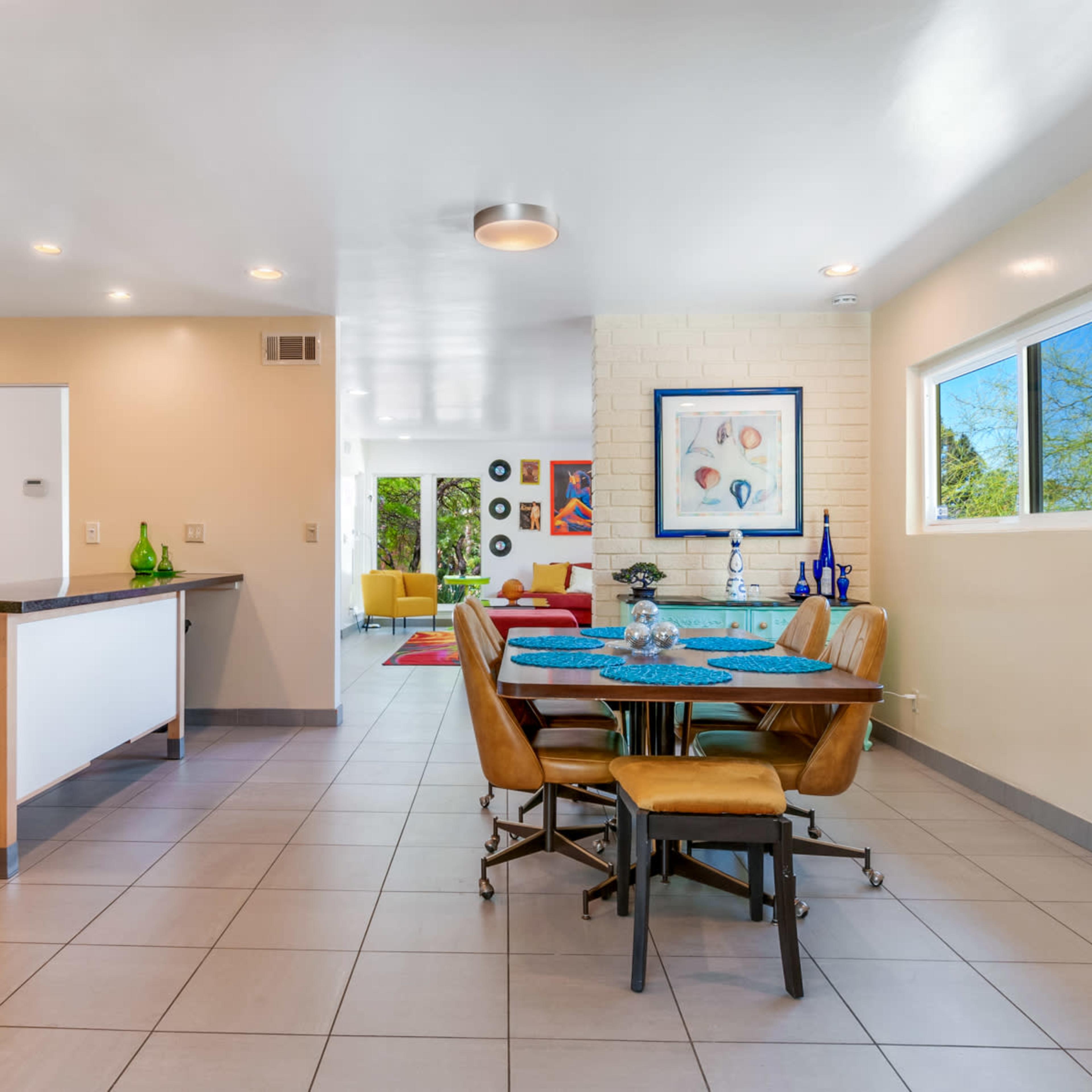 A modern, open-concept kitchen and dining area with a wooden table, four chairs, and a view into a brightly lit living space.