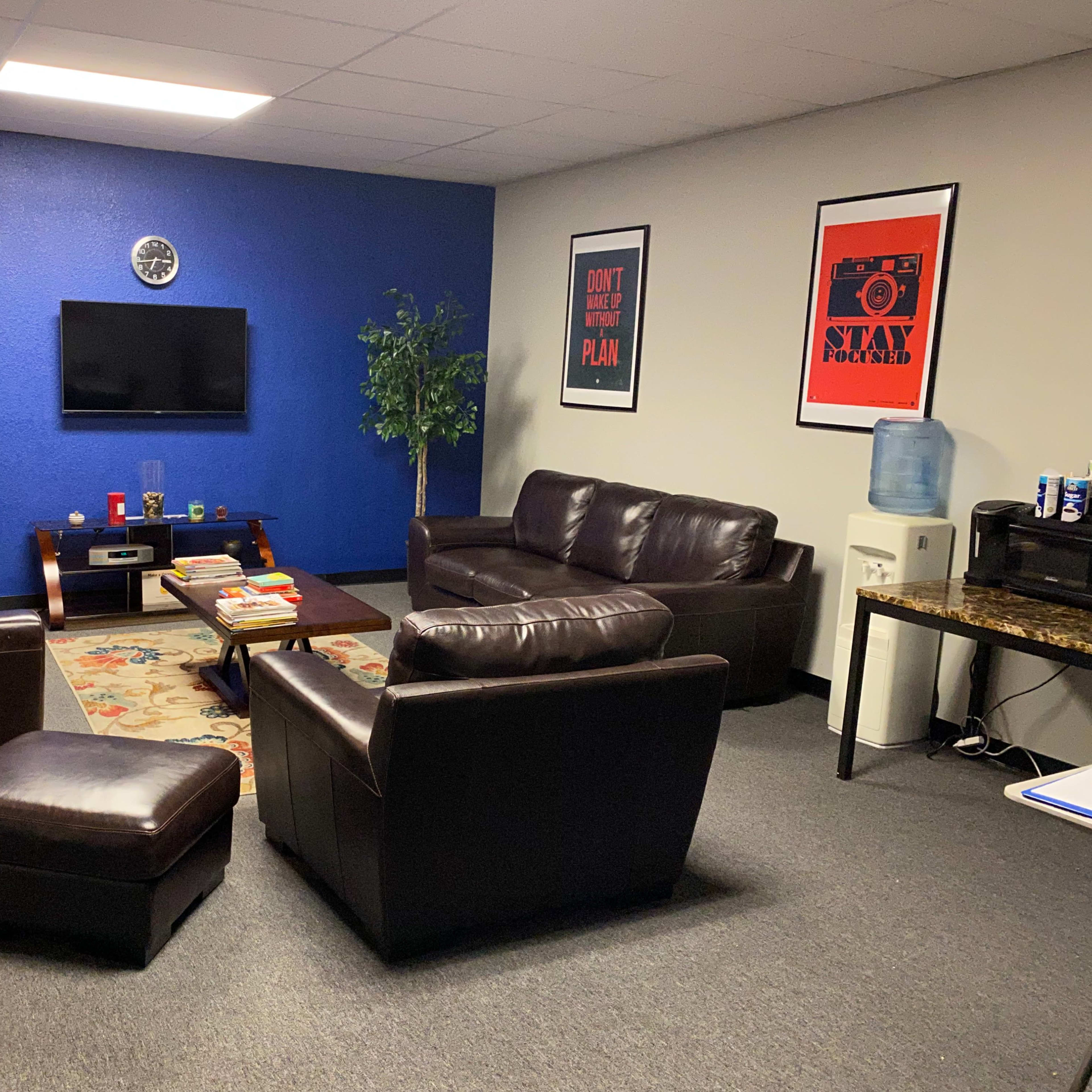 A seating area with brown leather sofas, an ottoman, a coffee table, a television mounted on a blue wall, and framed posters.