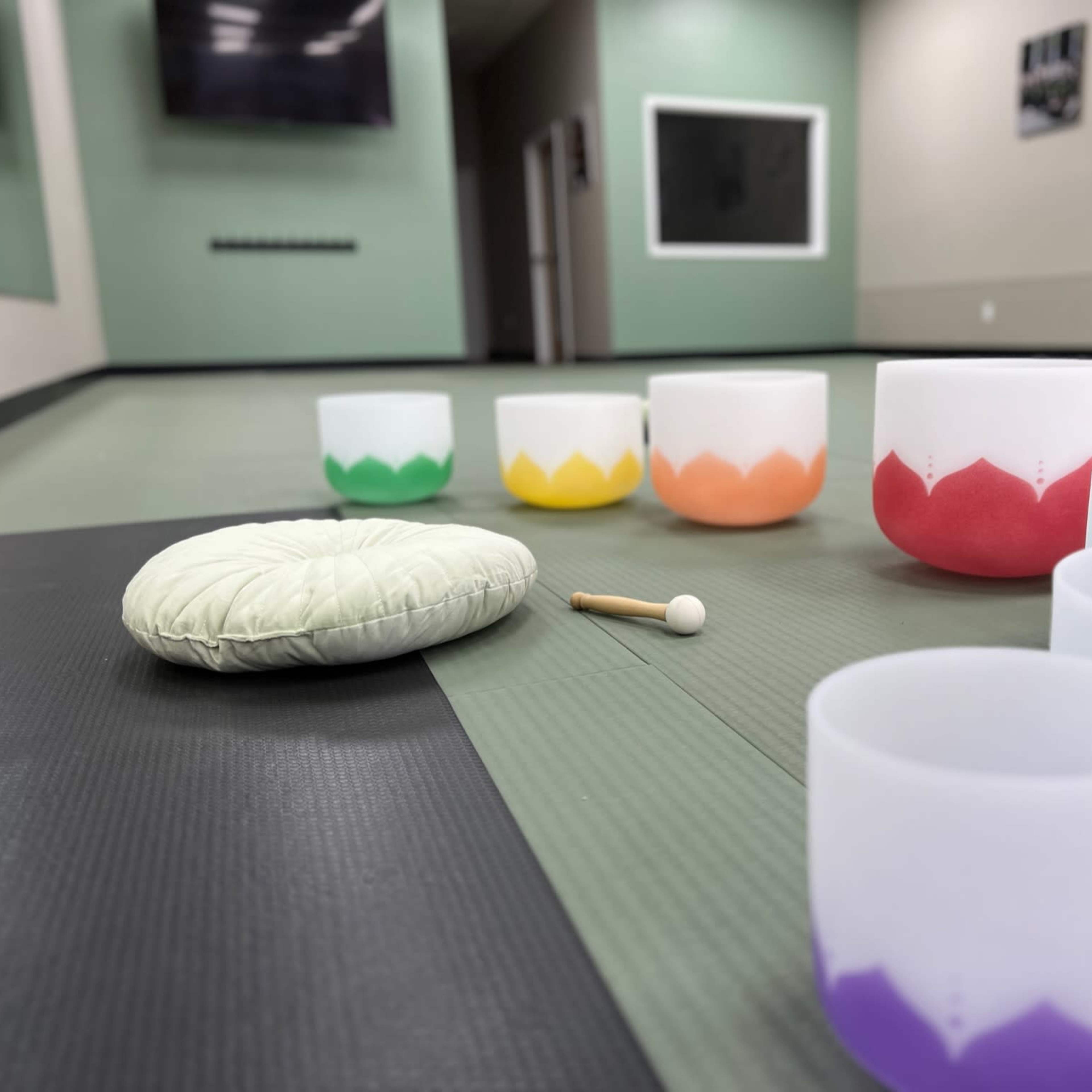 A collection of pastel-colored bowls arranged on a green rubber mat in a spacious room designed for relaxation or meditation.