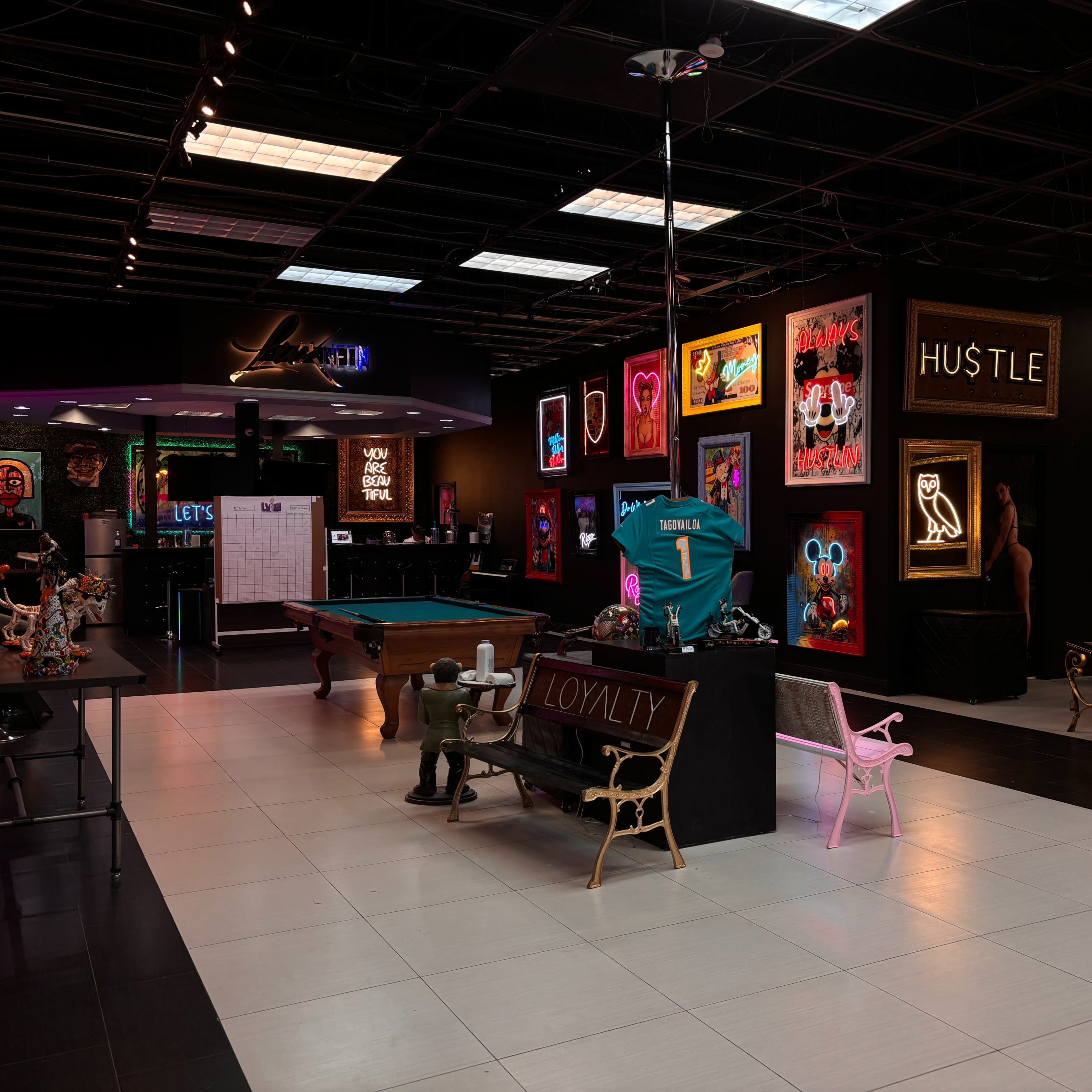 A stylish entertainment venue featuring a pool table, illuminated neon signs, and modern furniture arranged in an open layout.