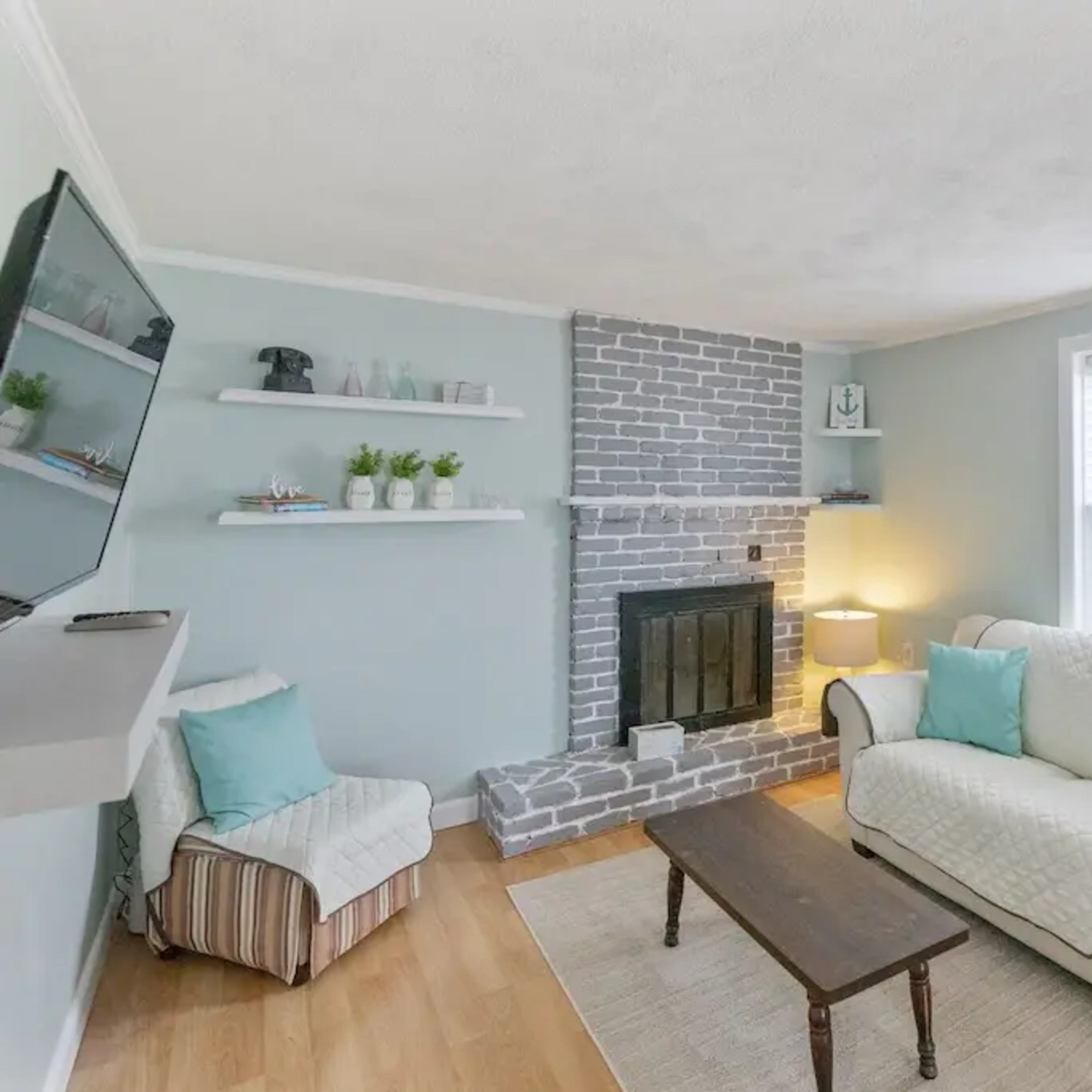 A small living room with a light blue color scheme, featuring a gray brick fireplace, a comfortable sofa, and a wooden coffee table.