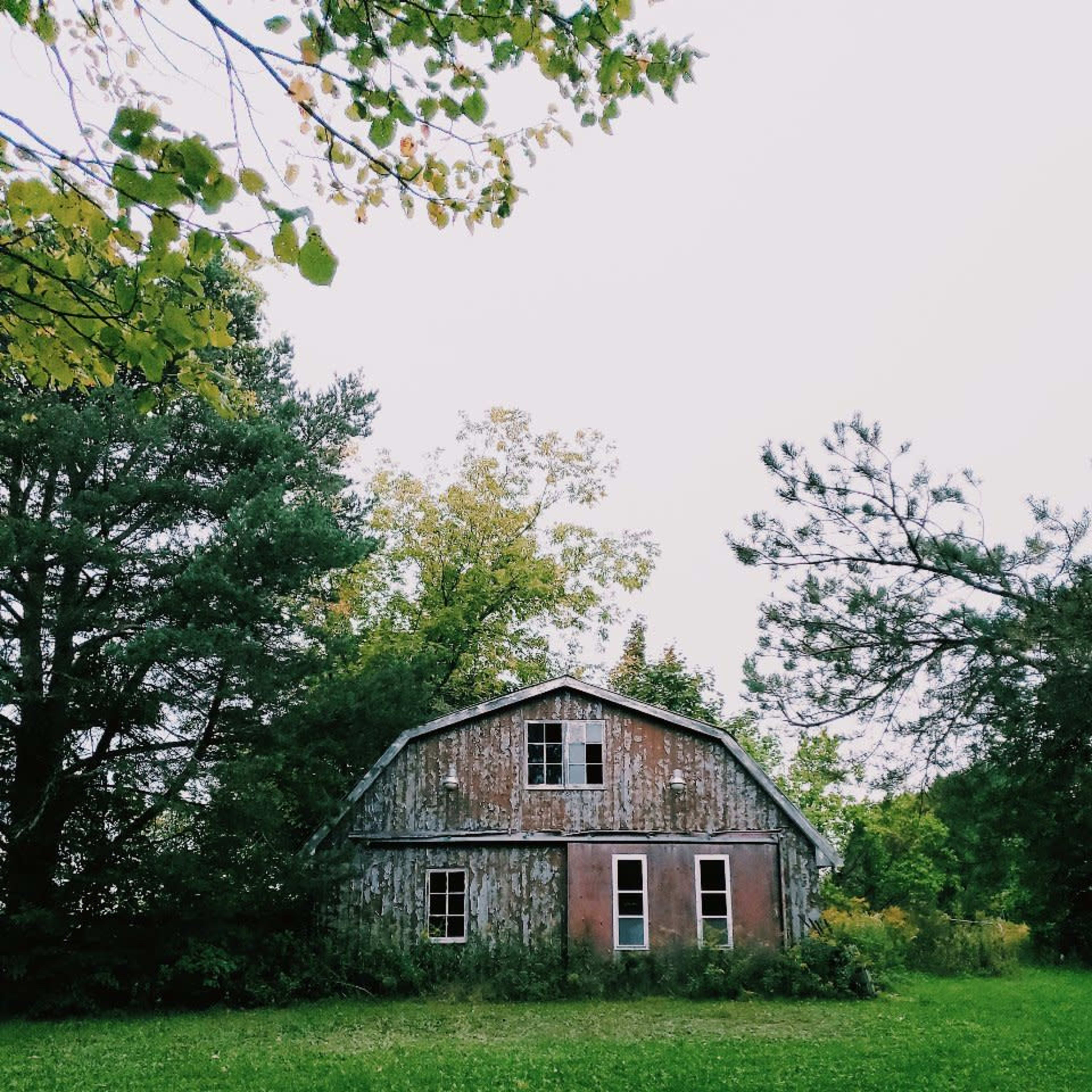 A weathered barn stands surrounded by trees on a grassy area.