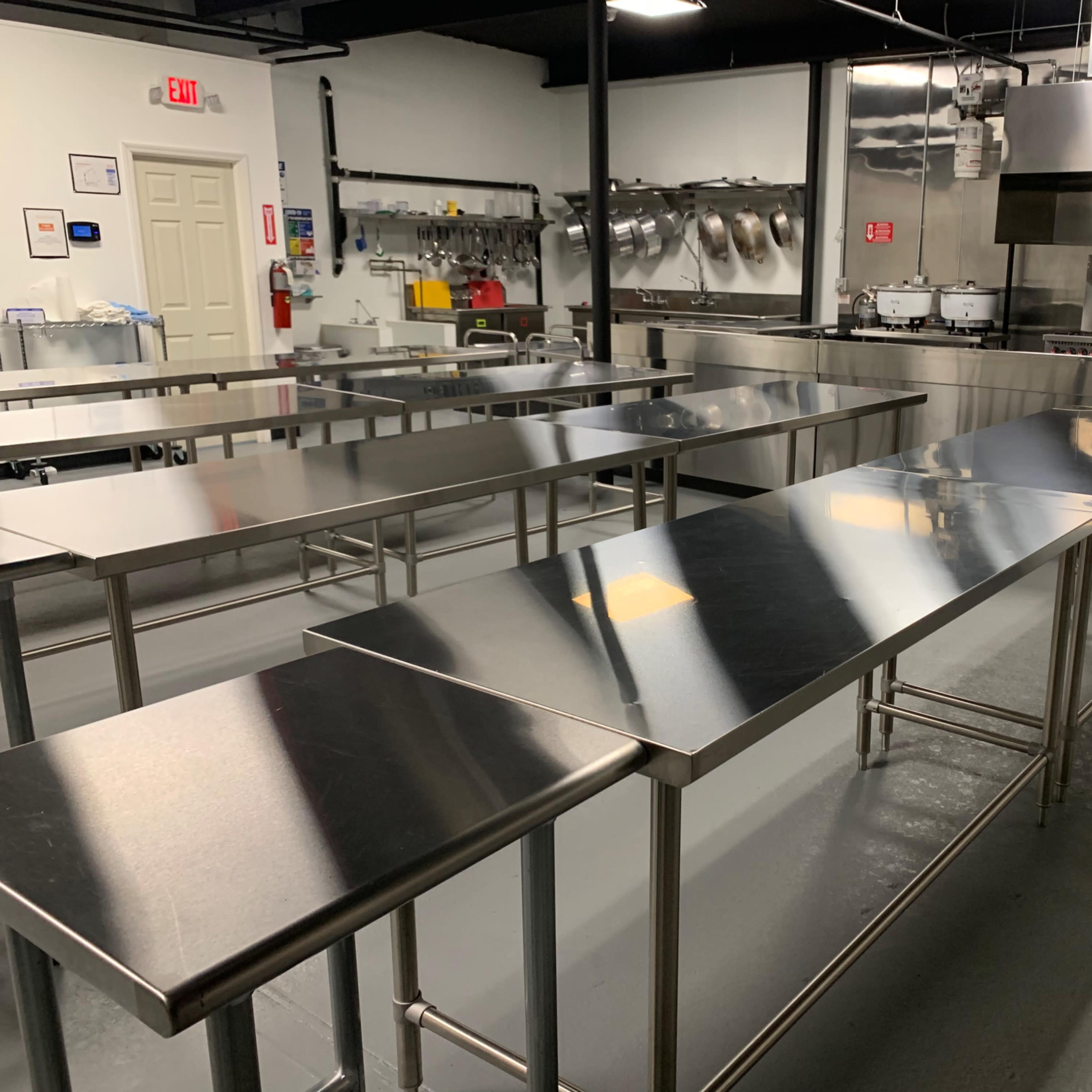 A commercial kitchen with several stainless steel tables and industrial cooking equipment.