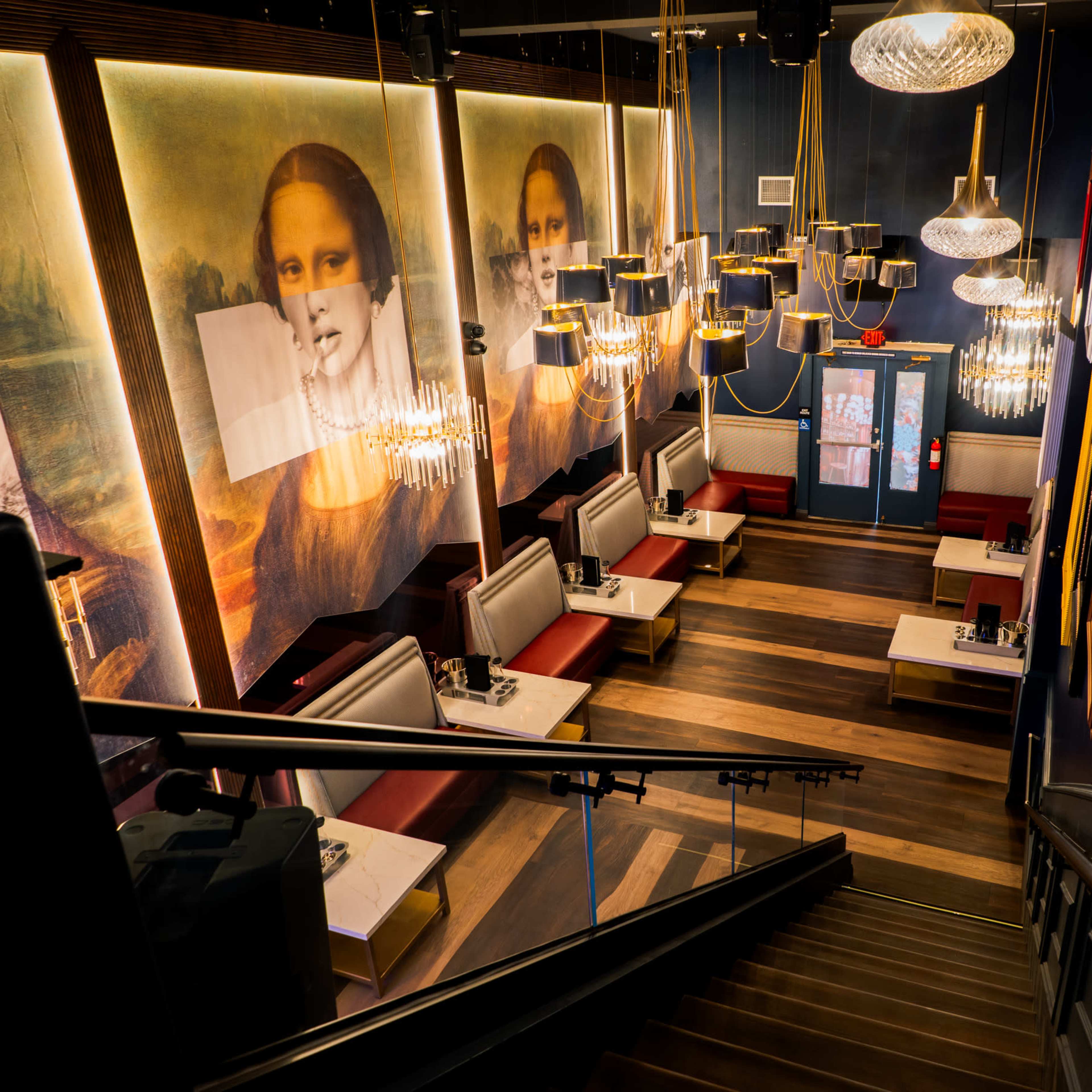 A restaurant interior featuring seating areas with white tables and red upholstered benches, highlighted by large portraits on the walls and decorative chandeliers.