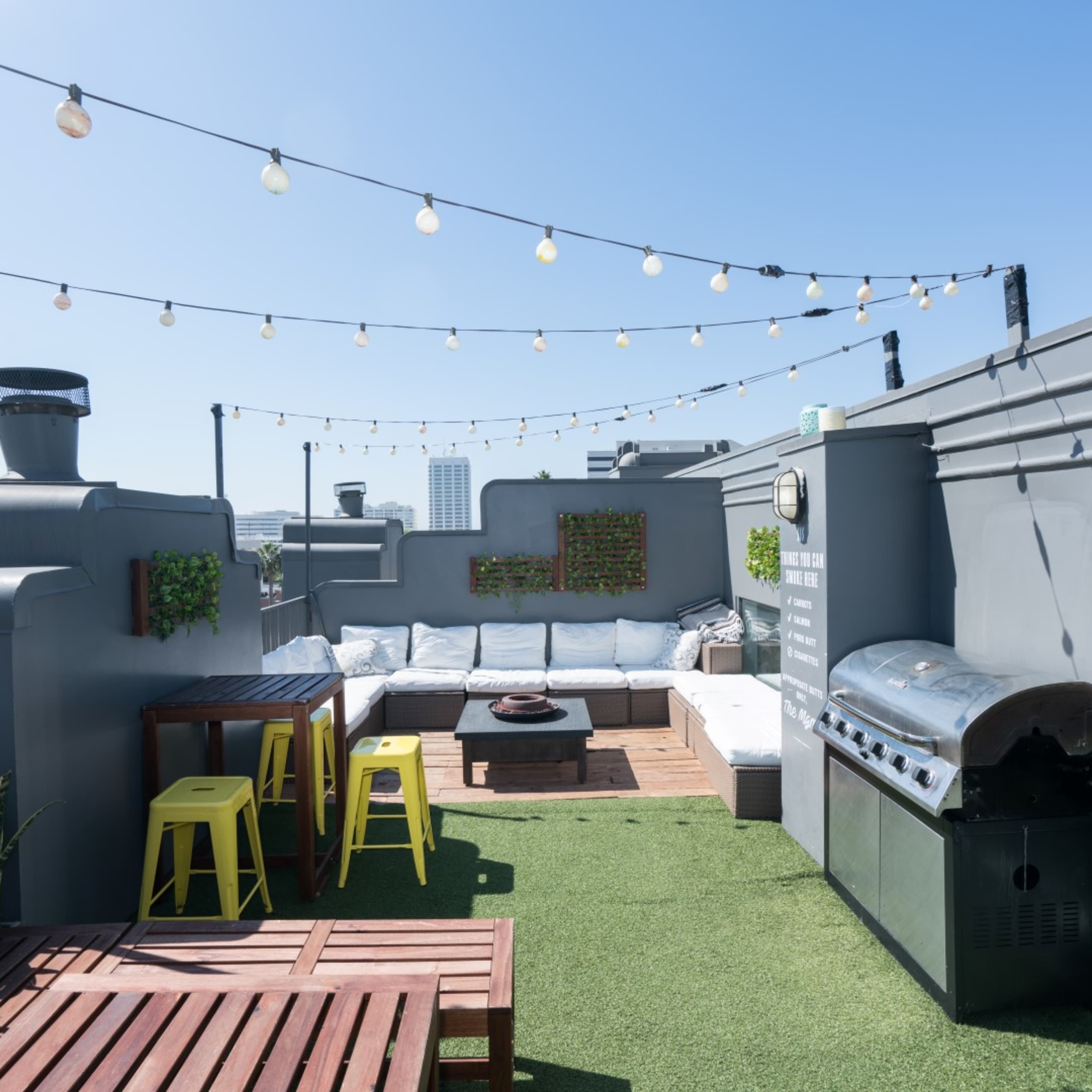 A rooftop terrace with string lights, a grill, a seating area, and wooden furniture.