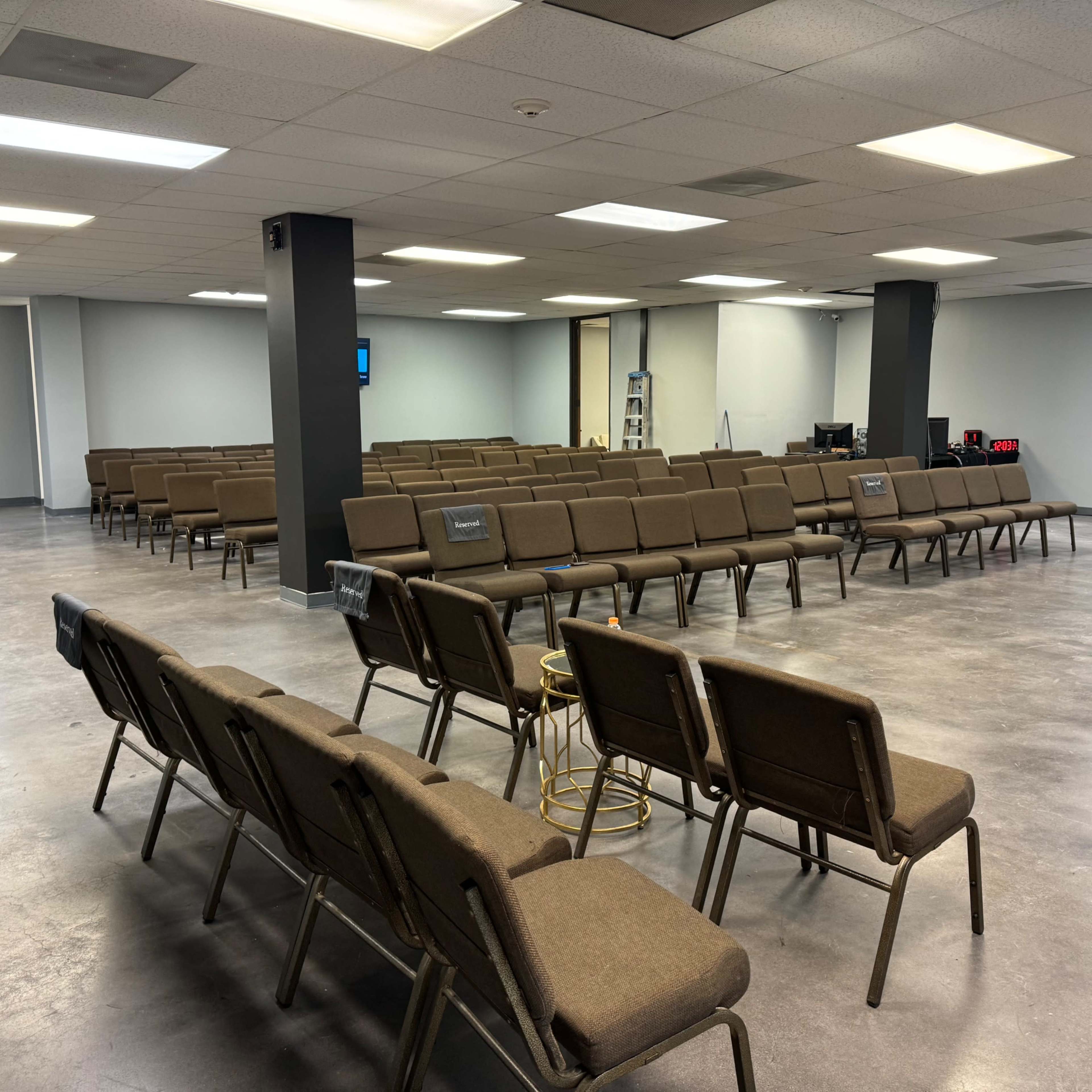 A large, empty room set up with rows of brown chairs facing a stage area.