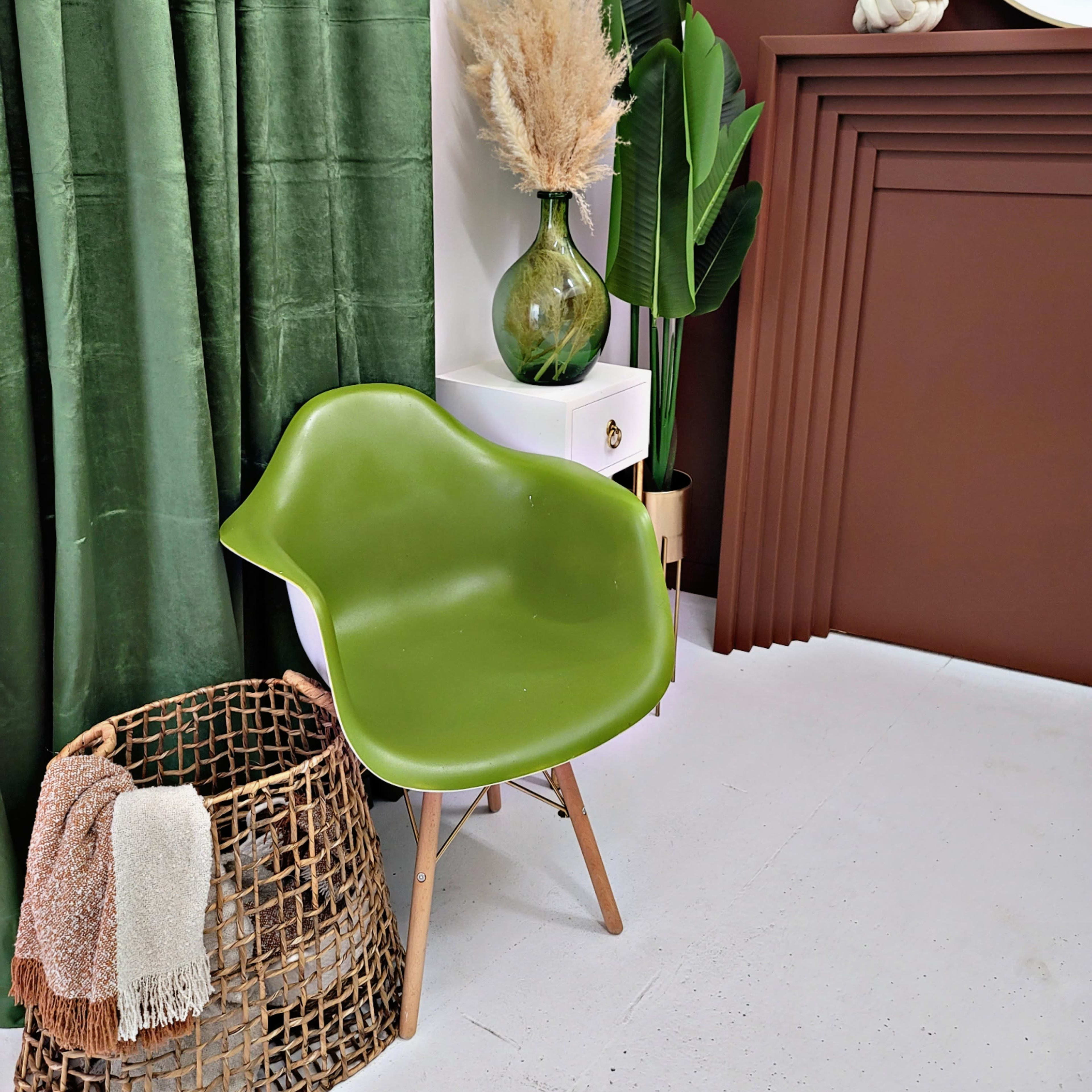 A green chair beside a woven basket, with green curtains, a decorative vase containing dried plants, and a brown accent wall.