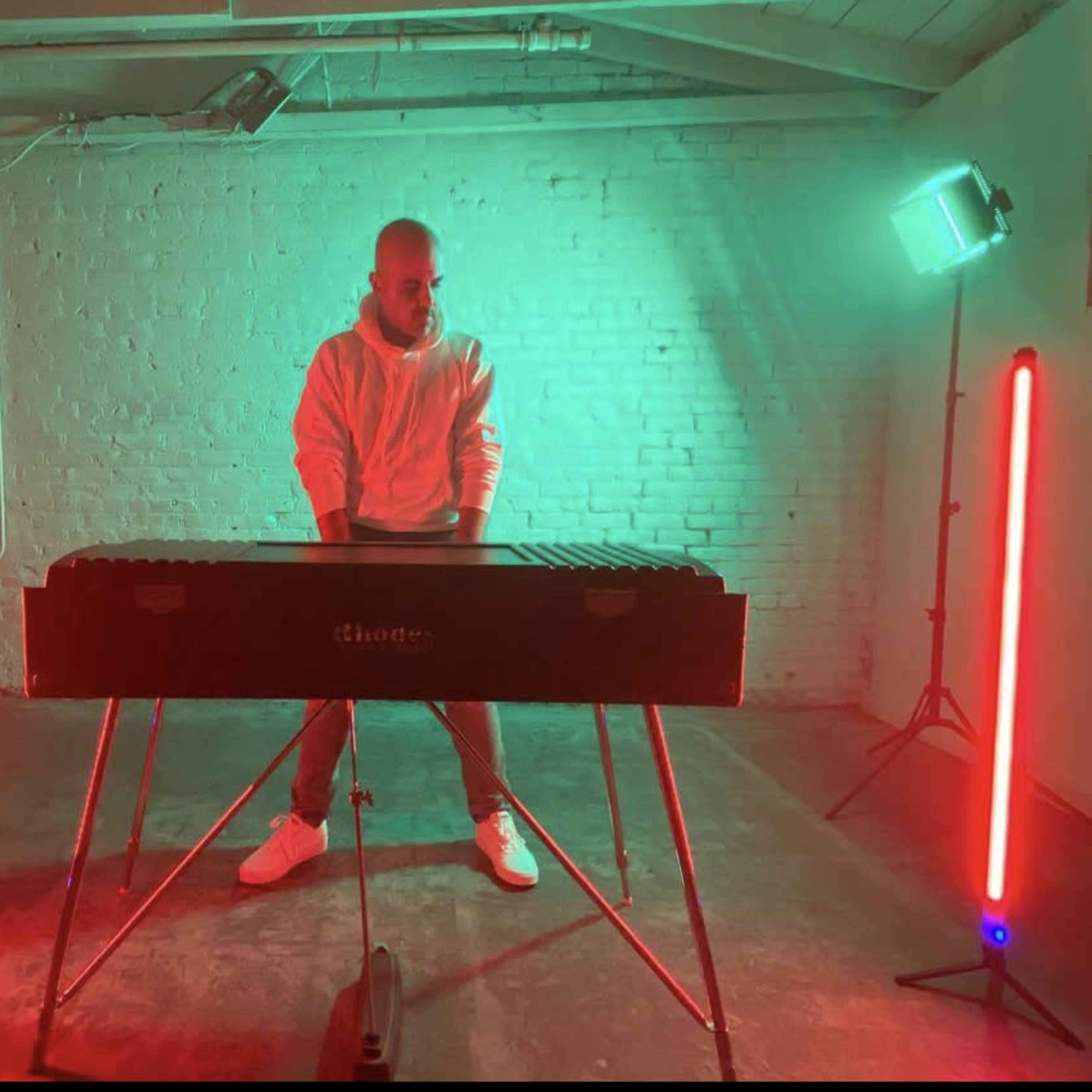 A musician stands in front of a xylophone, surrounded by red and green lights in an industrial setting.