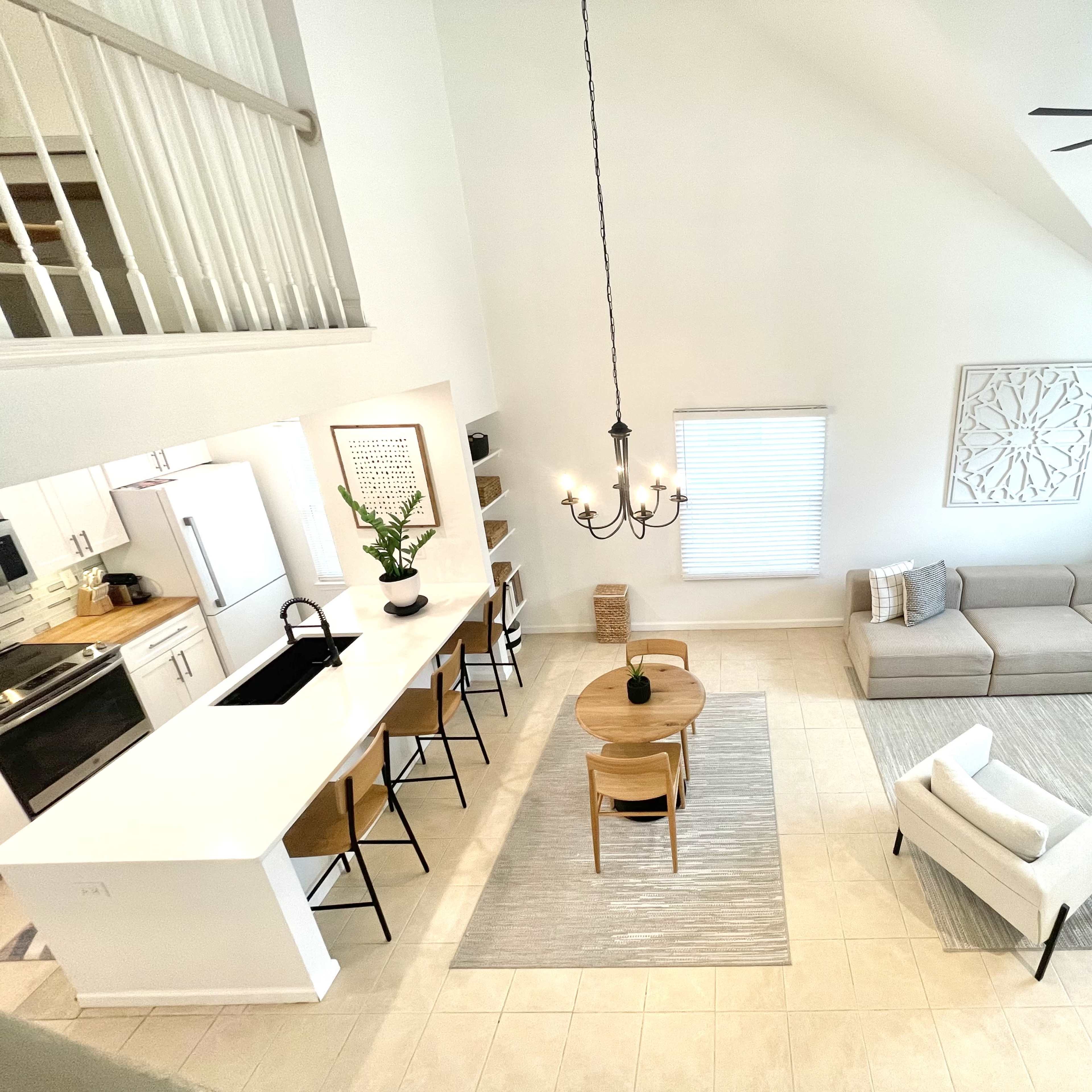 A spacious, modern living room and dining area with a neutral color palette, a large sectional sofa, a round dining table, and tall windows allowing natural light.
